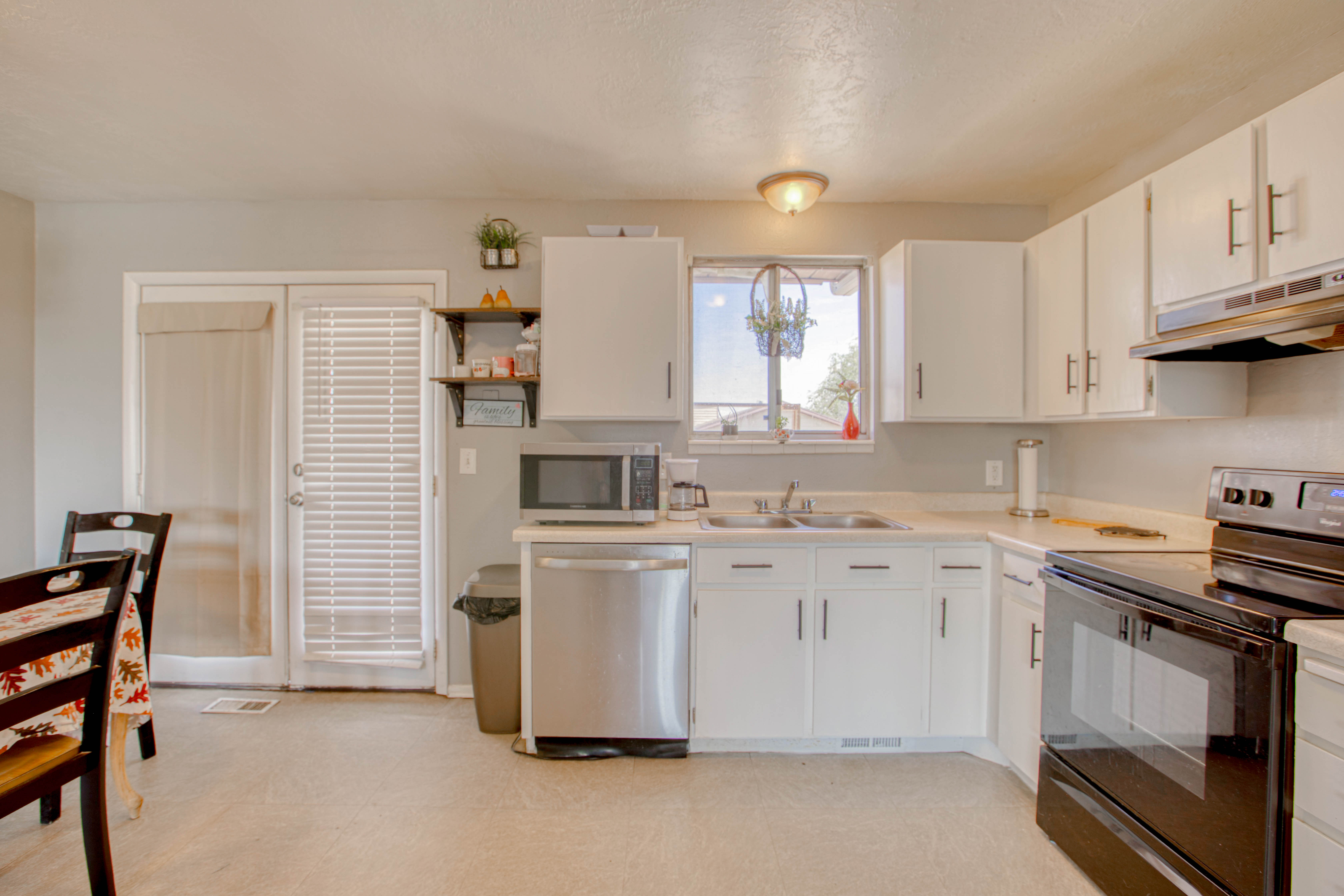 Kitchen featuring white cabinetry with brushed nickel hardware, a stainless steel dishwasher, a double basin sink beneath a window, and a range with an overhead microwave