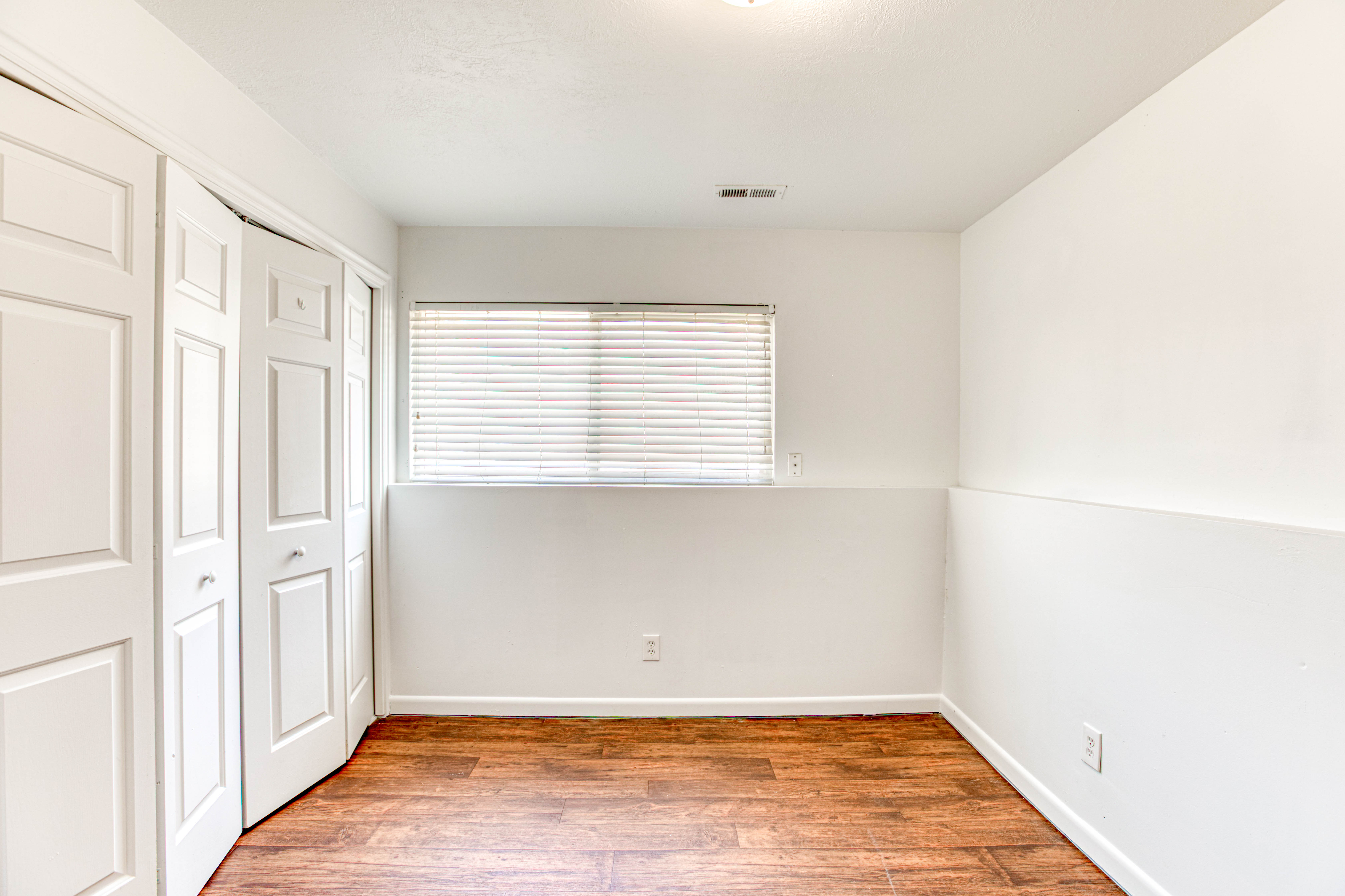 Room featuring wood-finish flooring, a window with blinds, and bi-fold closet doors