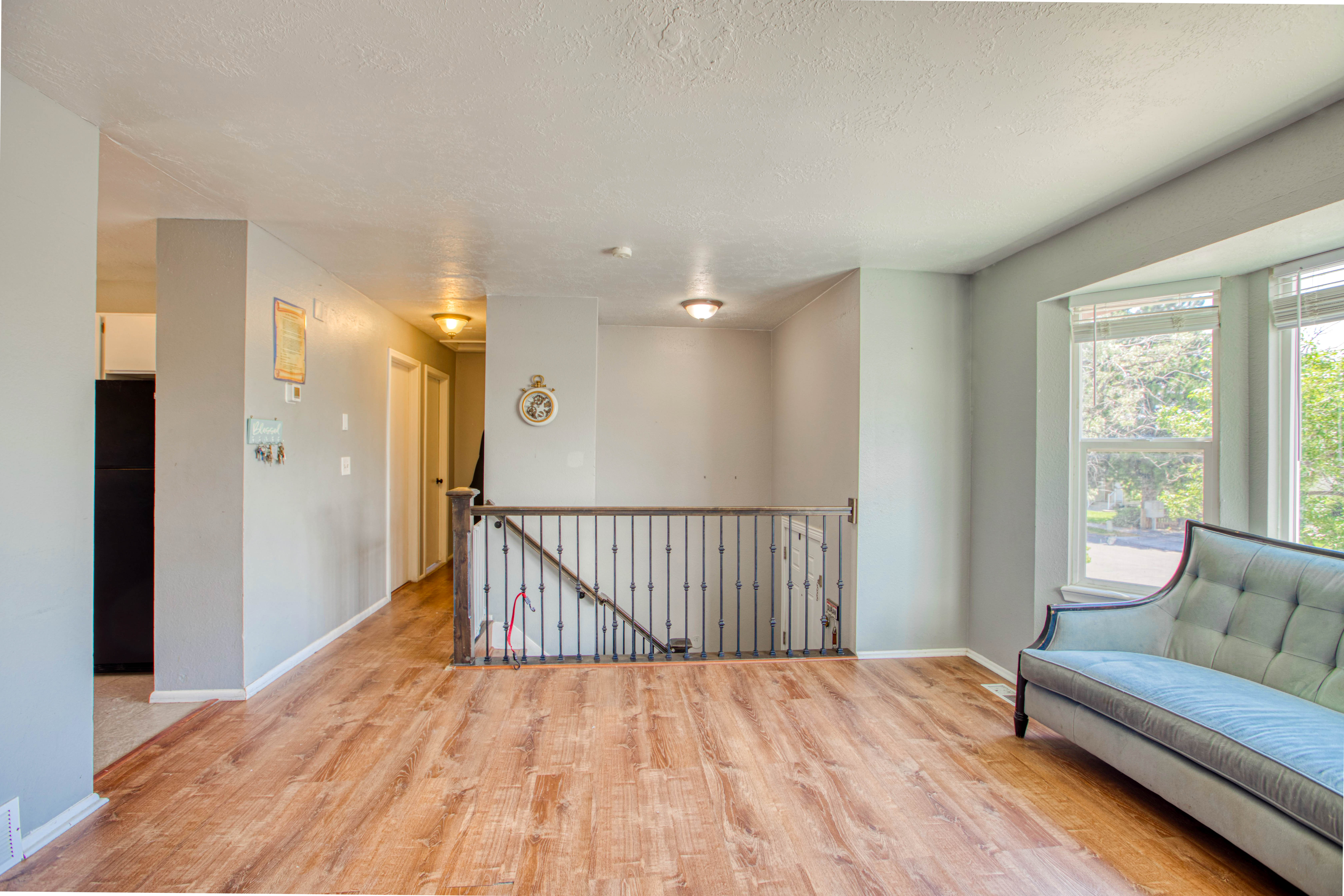 Expansive room featuring wood-finish flooring, a decorative metal railing, and a bay window