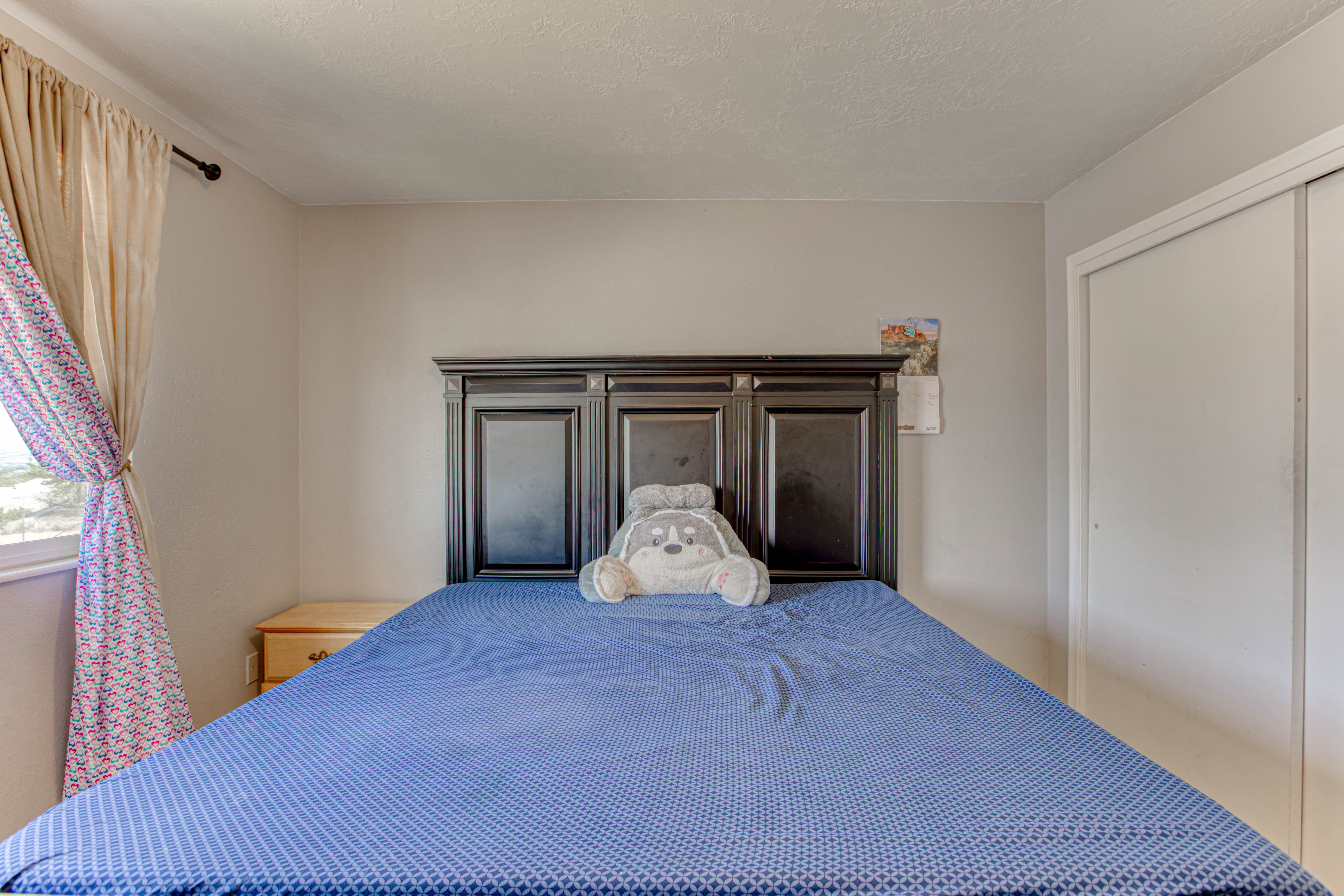 Spacious room featuring a dark wood-finish headboard, a window with curtains, and a built-in closet with sliding doors
