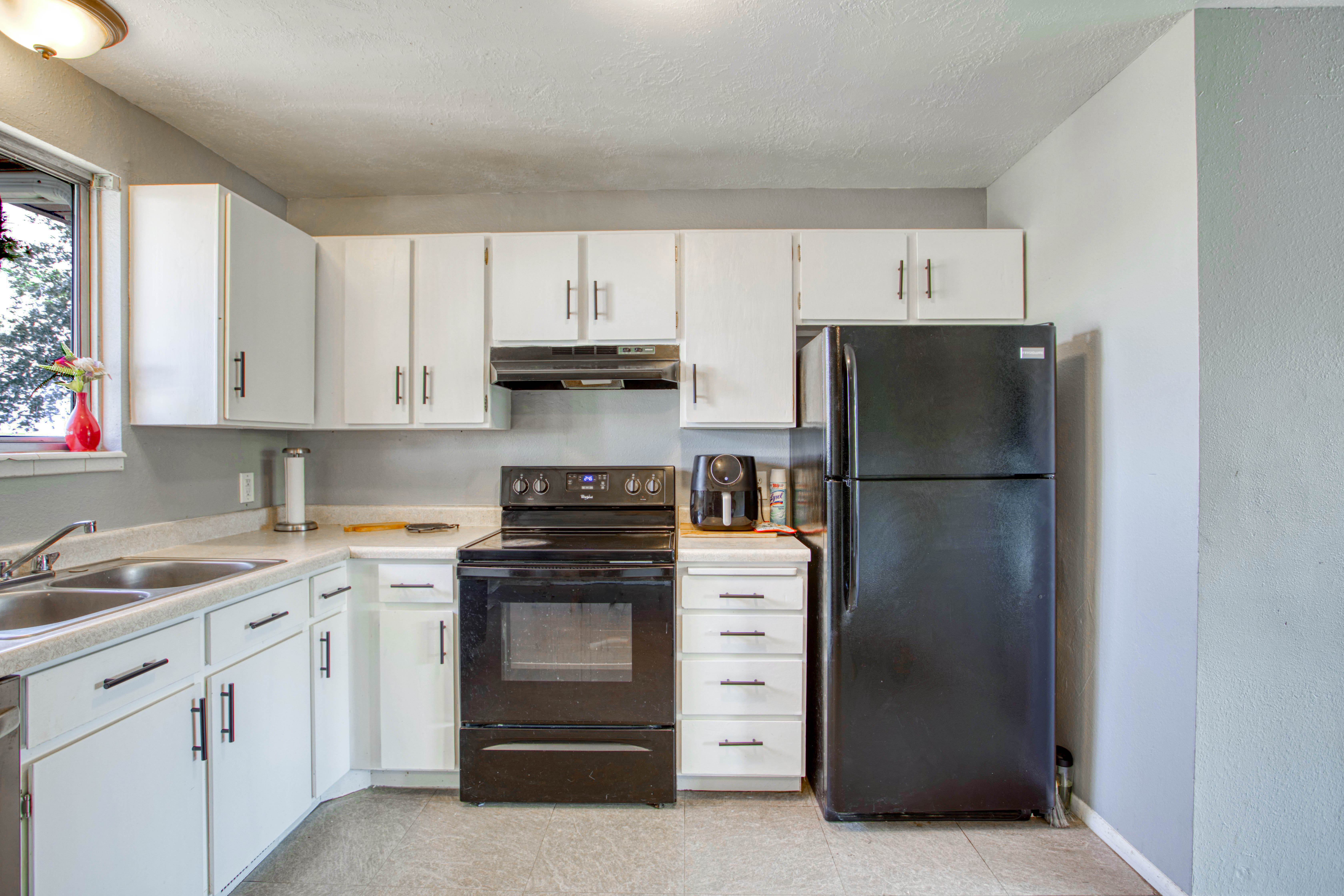Kitchen featuring white cabinetry with dark hardware, a black electric range, a black refrigerator, a double basin sink, and wood-finish flooring