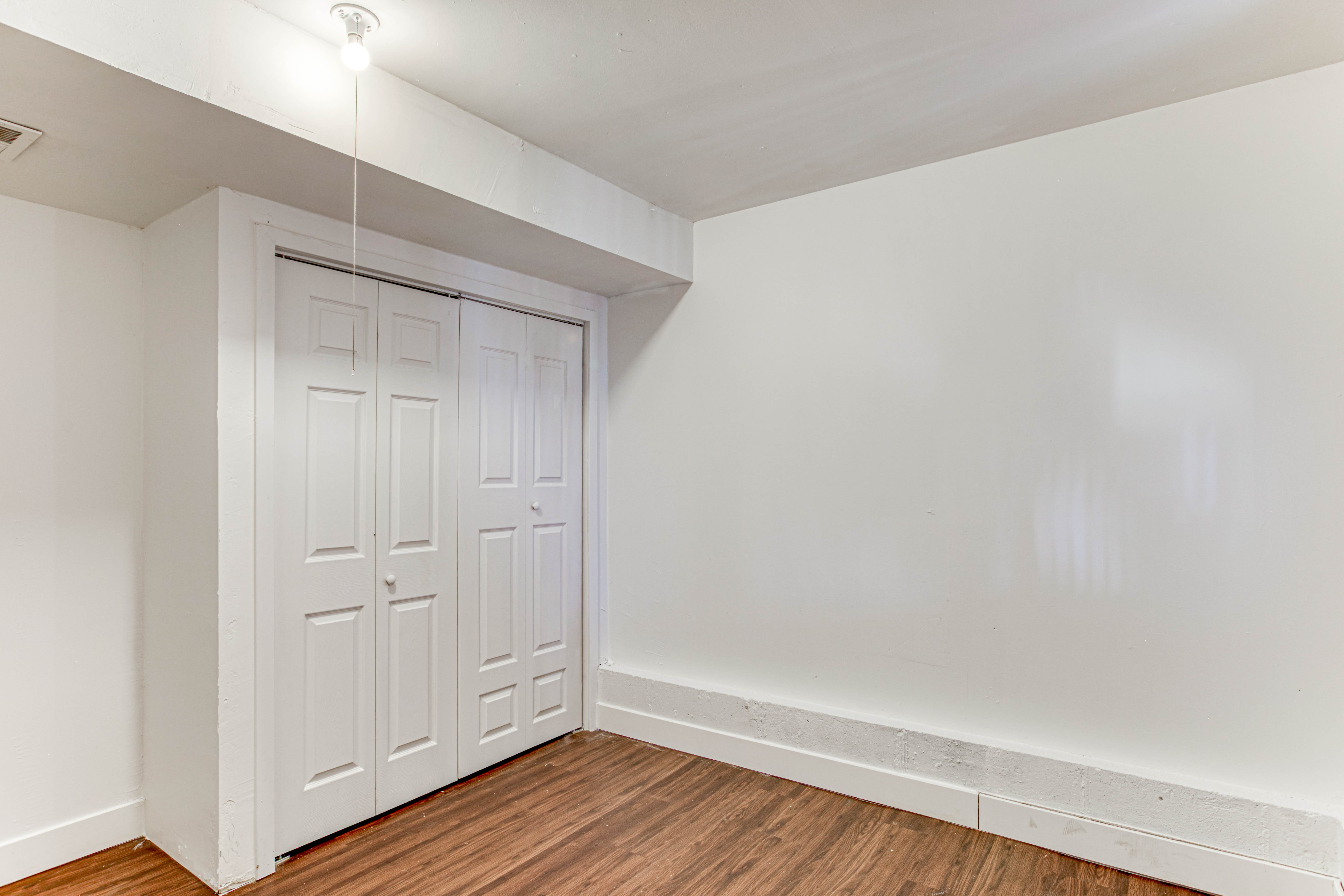 Room featuring wood-finish flooring, white painted walls, and a white bi-fold closet