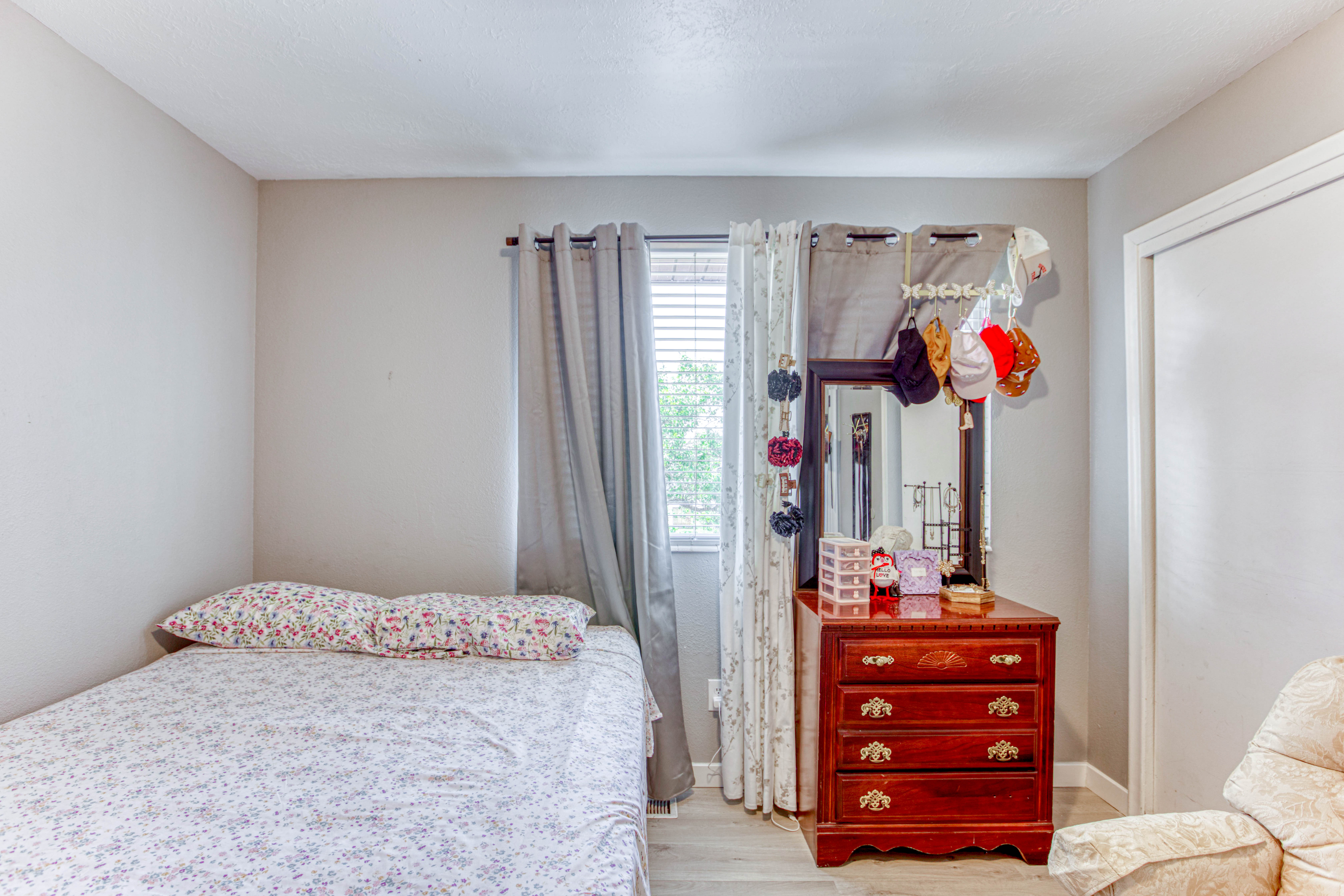 Bright room featuring light-colored walls, wood-finish flooring, and a window with blinds and curtains