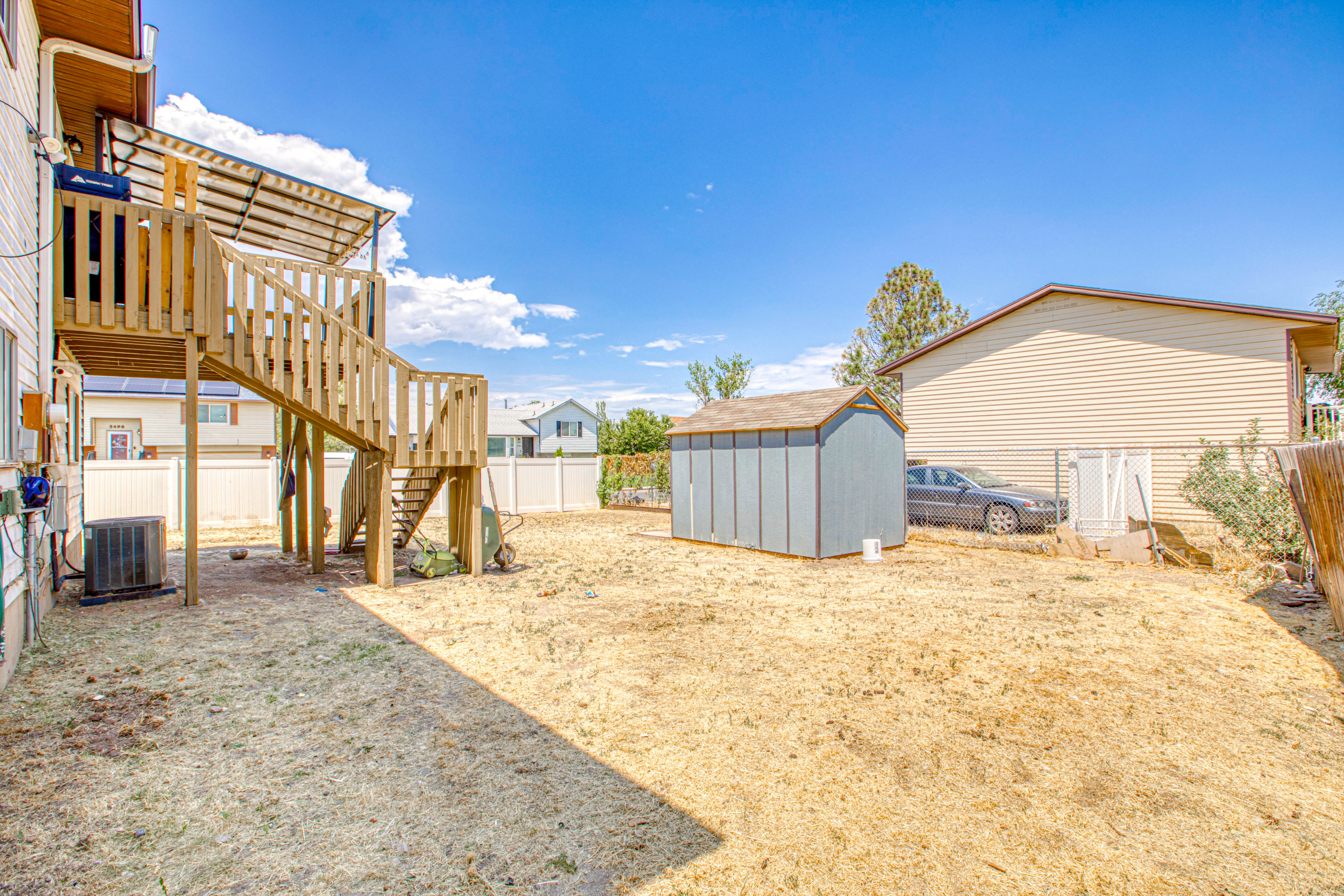 Spacious backyard featuring a multi-level wooden deck with stairs, a detached storage shed, and a privacy fence