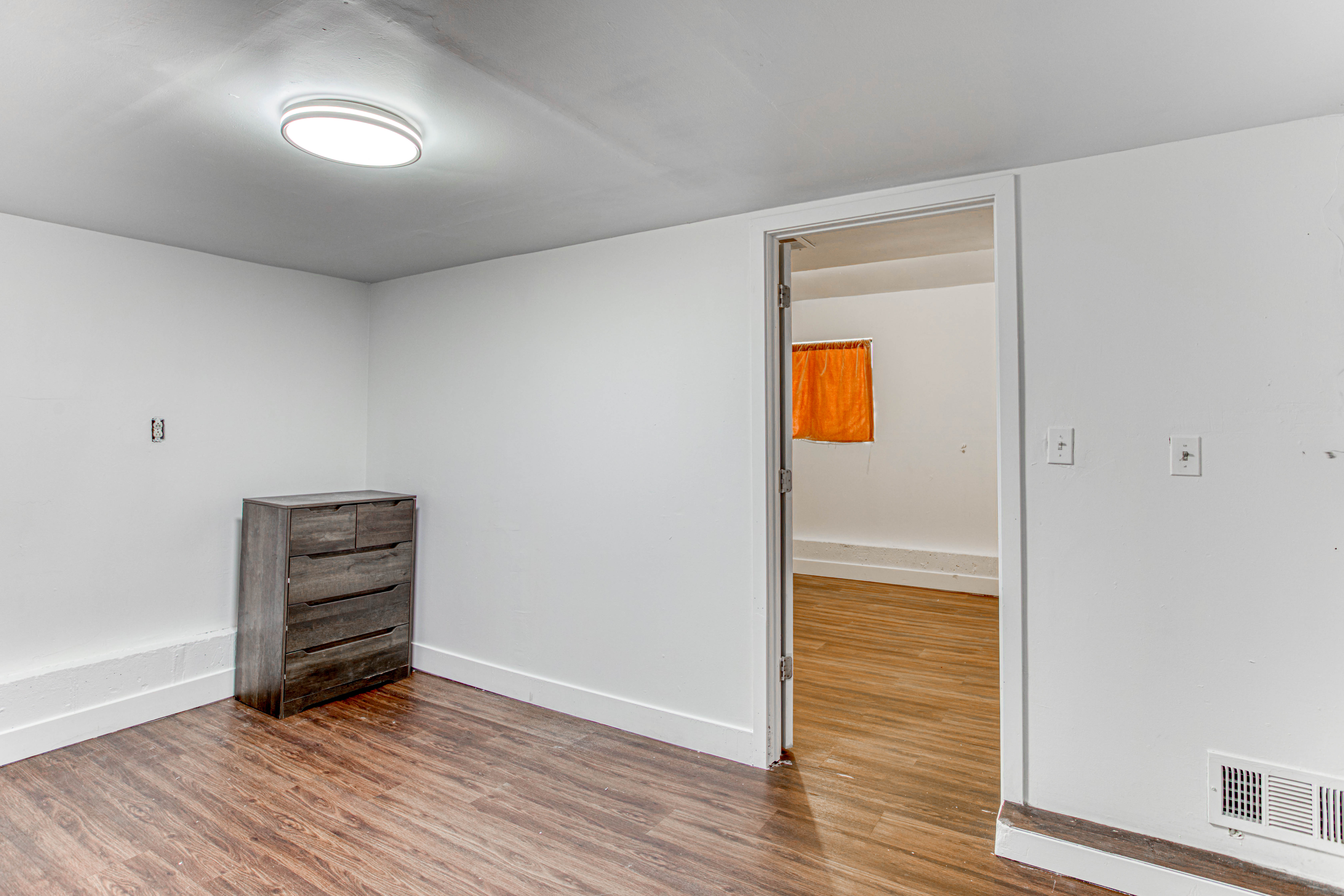 Room featuring wood-finish flooring, white painted walls, and a contemporary ceiling light fixture