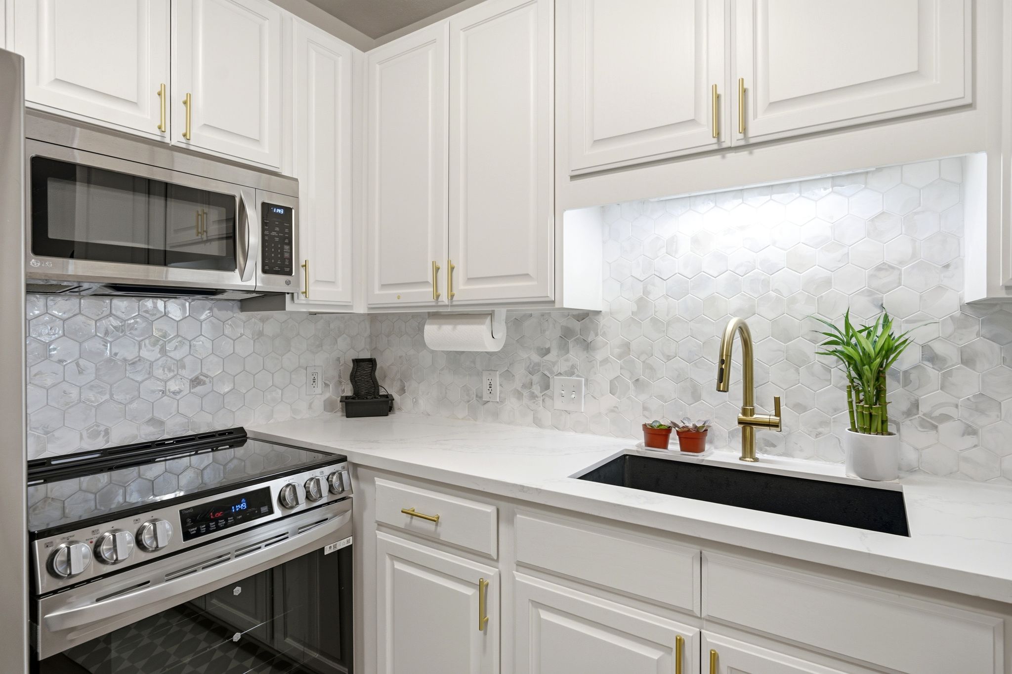 Kitchen featuring new range and garbage disposal, white cabinetry, gold-tone hardware, stainless steel appliances, a white hexagonal tile backsplash, and a black undermount sink with a gold-tone faucet
