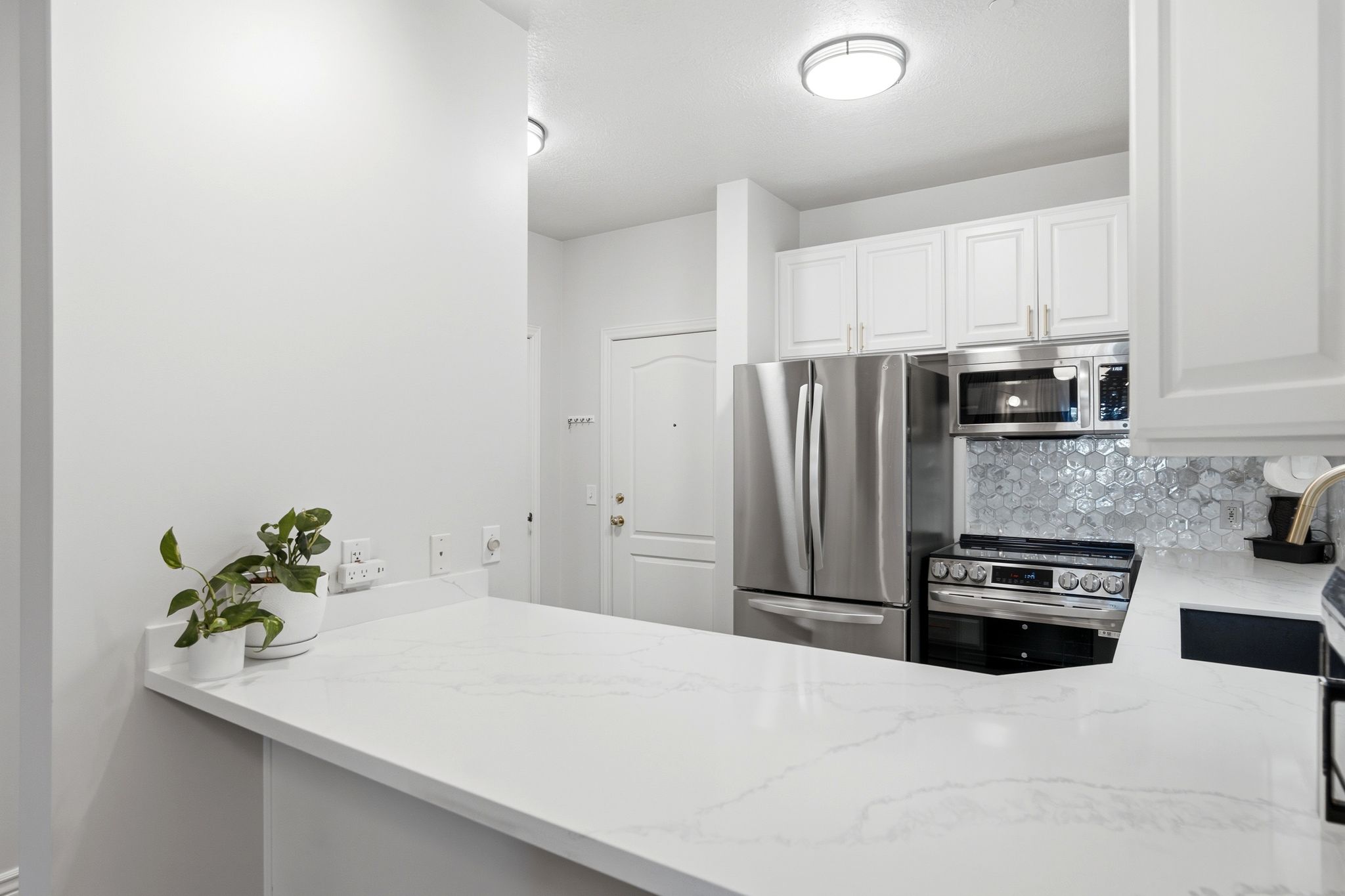 The kitchen sits just inside the front door with stainless steel appliances, beautiful tile backsplash, and light-toned quartz countertops.