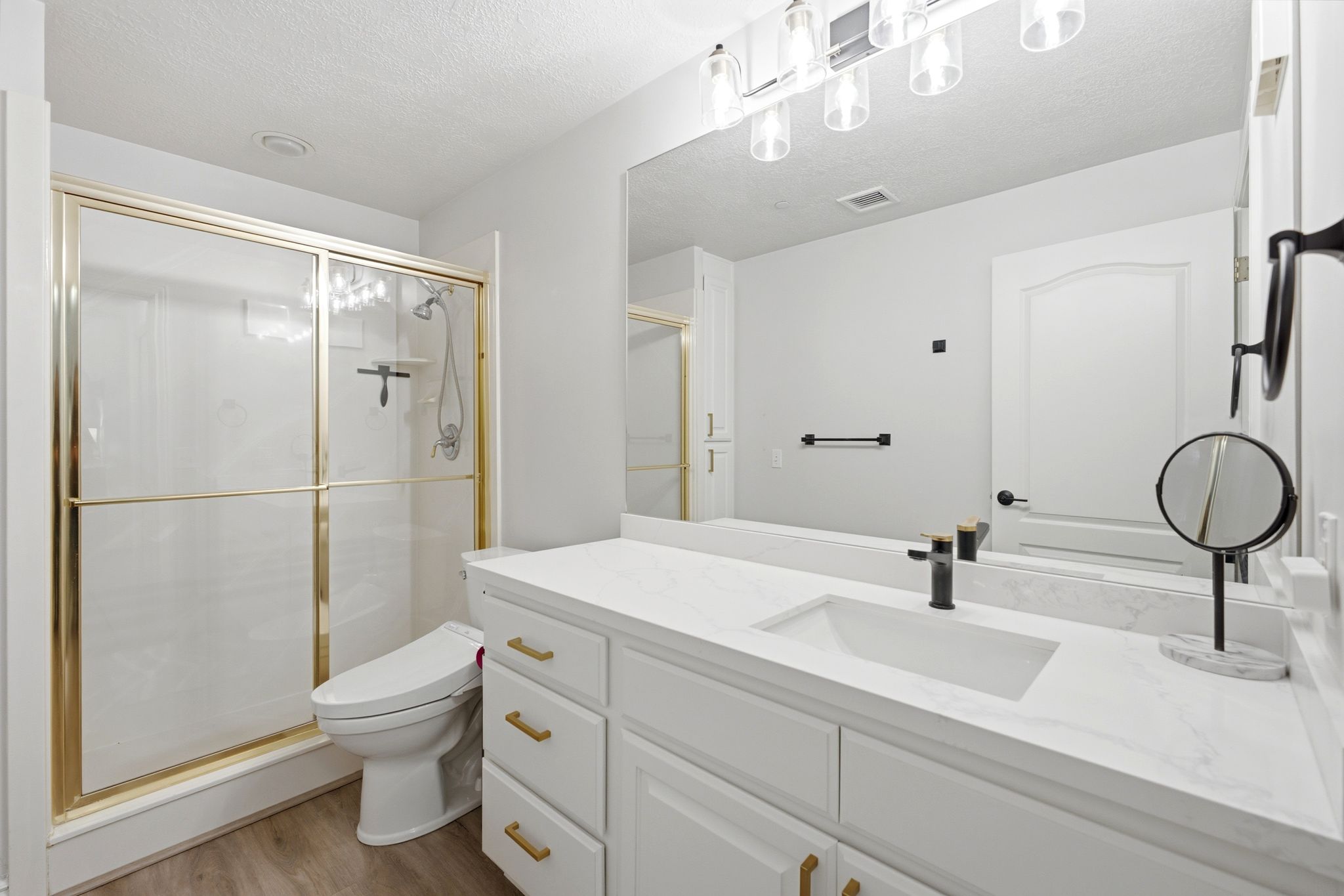 Primary bathroom featuring a updated quartz countertops, sink and fixture, gold-framed glass shower enclosure.