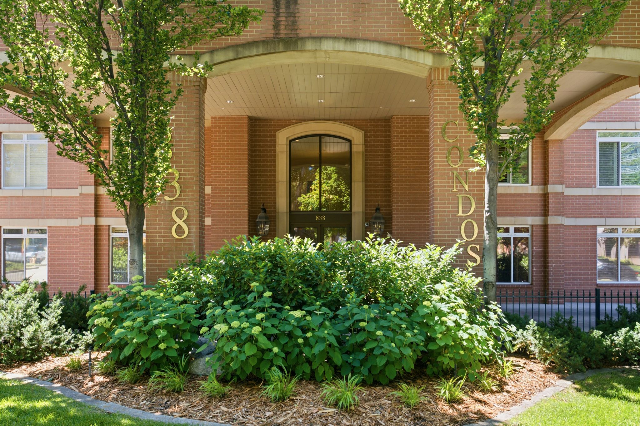 Welcome to city living! Entrance is accented with brick facade and a prominent arched entry, flanked by mature trees and lush landscaping. Controlled access entry.
