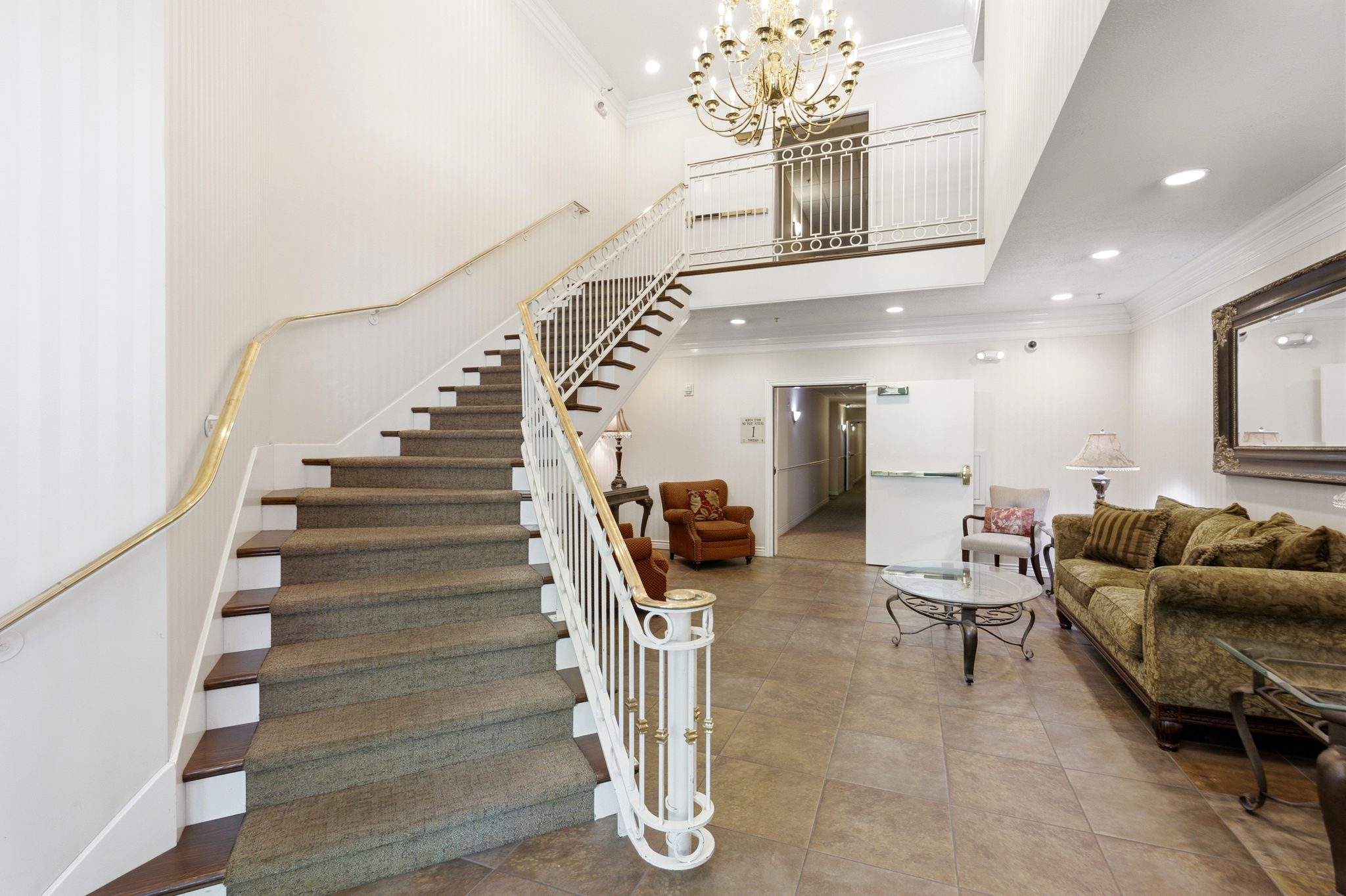 Grand entry foyer featuring a sweeping carpeted staircase with white balusters and brass handrails. Straight down the first level hallway to unit 107.