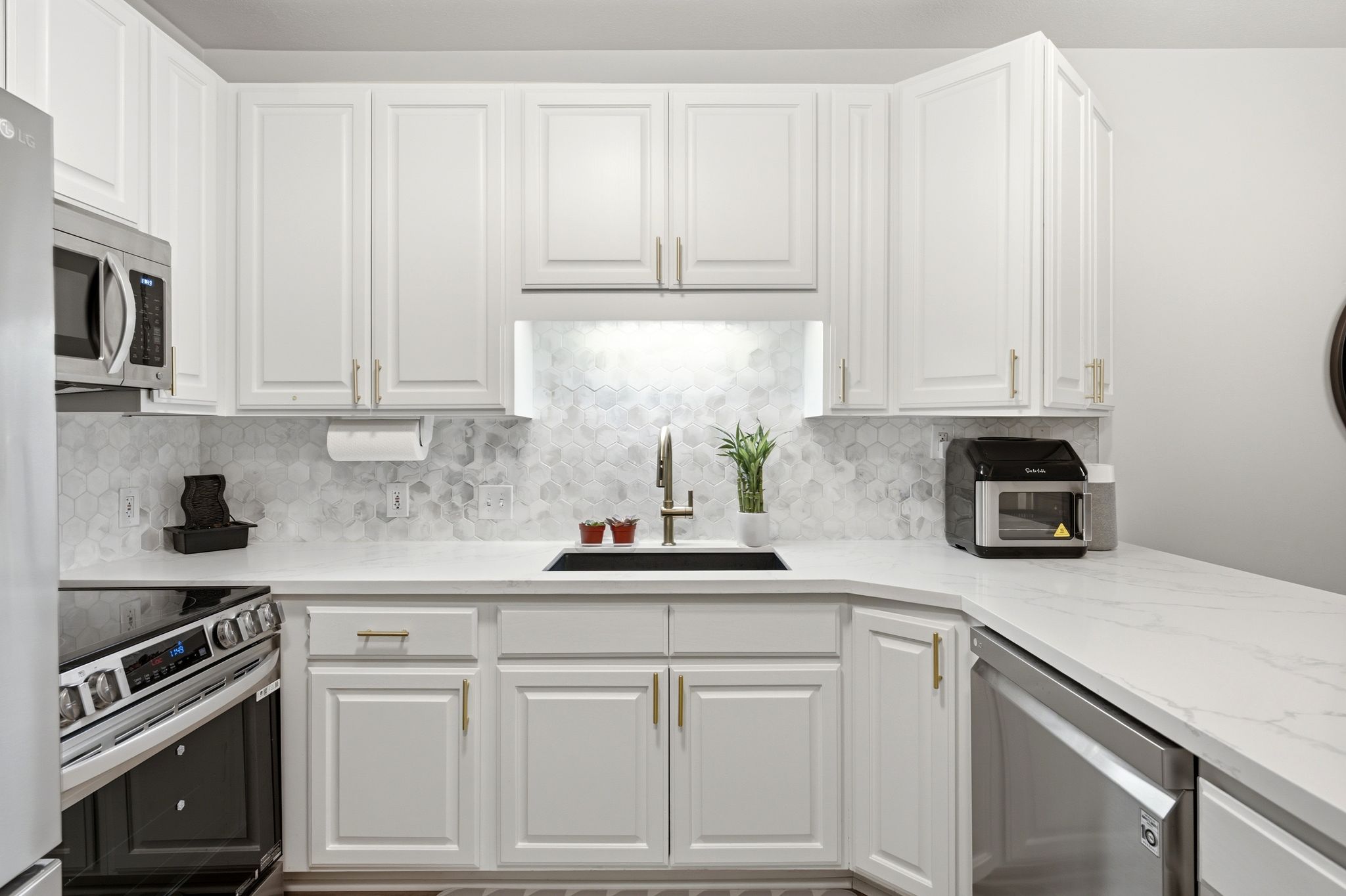 Modern kitchen featuring white shaker cabinetry with gold-tone hardware, stainless steel appliances, backsplash and quartz countertops.