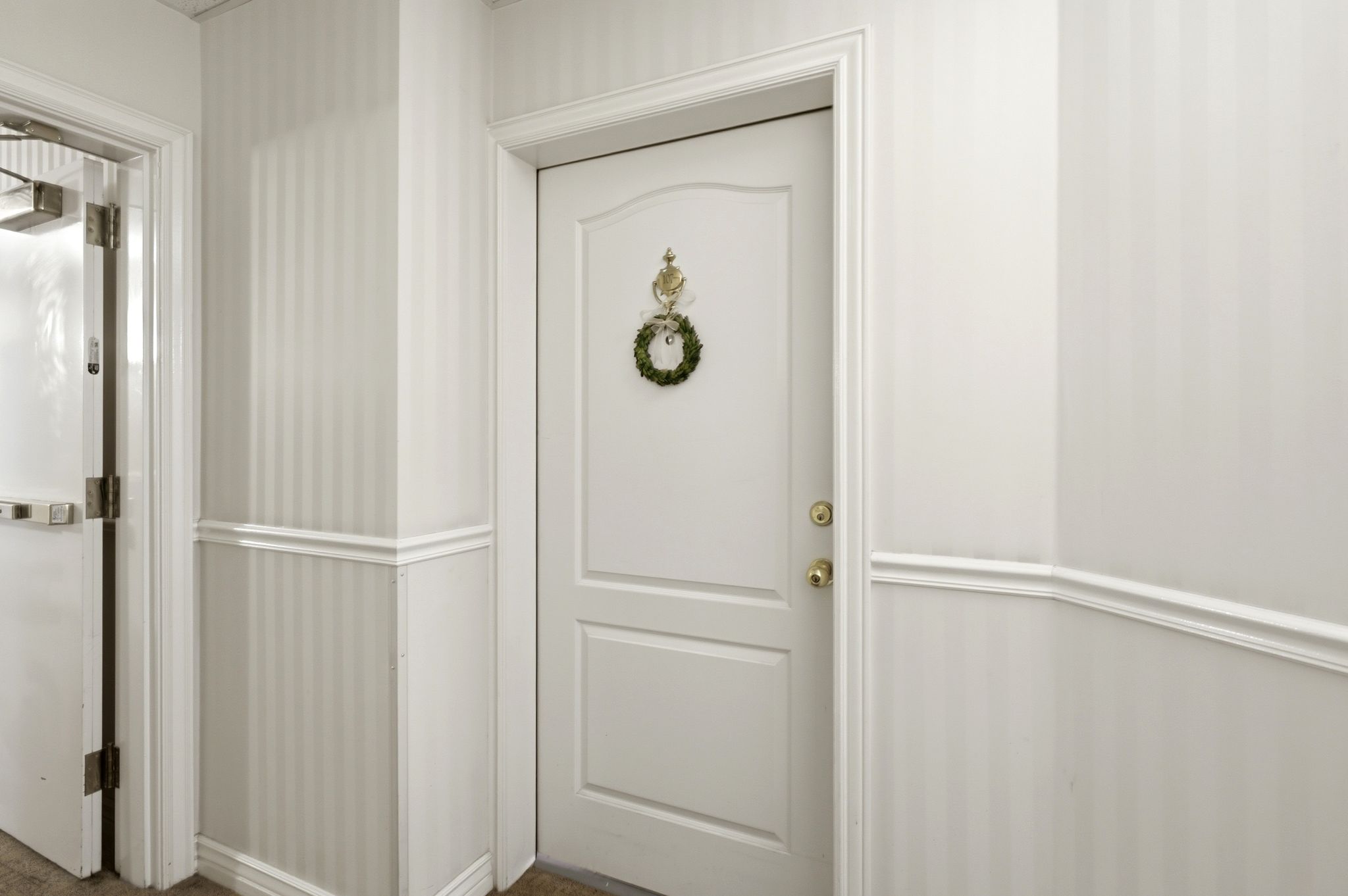 Welcome home! Entrance to condo 107. Interior door with brass hardware, framed by white millwork and striped wallpaper above wainscoting