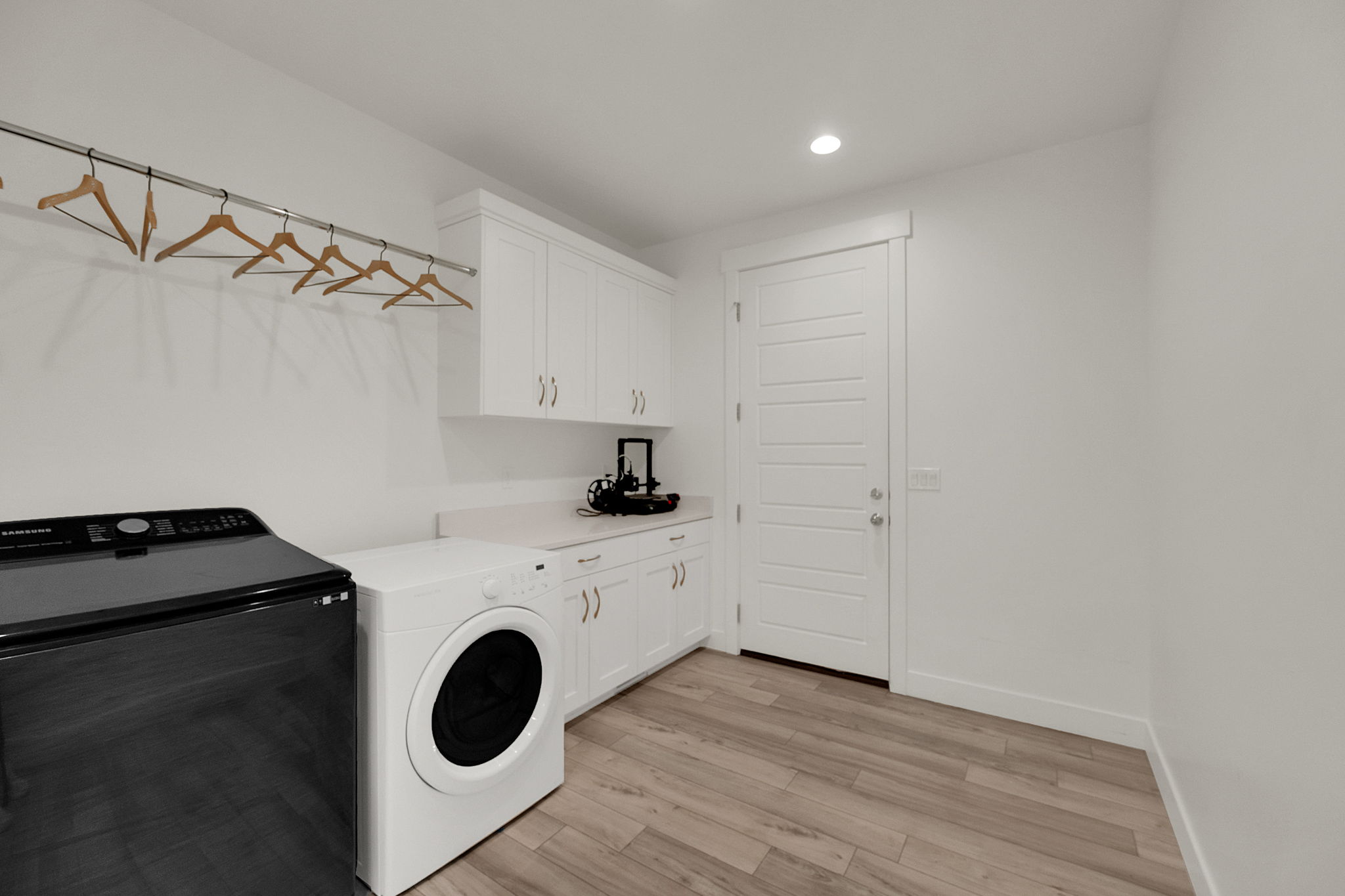 Laundry area featuring wood-finish flooring, white cabinetry, integrated countertop, and a clothes hanging rod