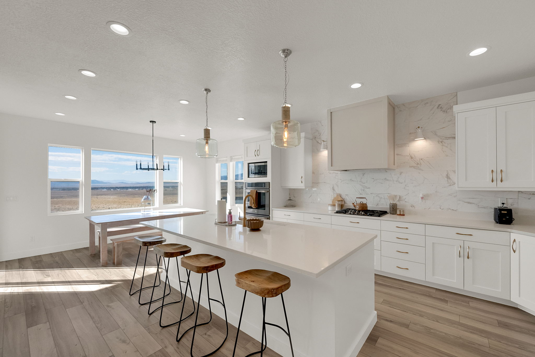 Bright kitchen featuring recessed lighting, a large central island with seating, white cabinetry, integrated appliances, and a full-height marble-effect backsplash