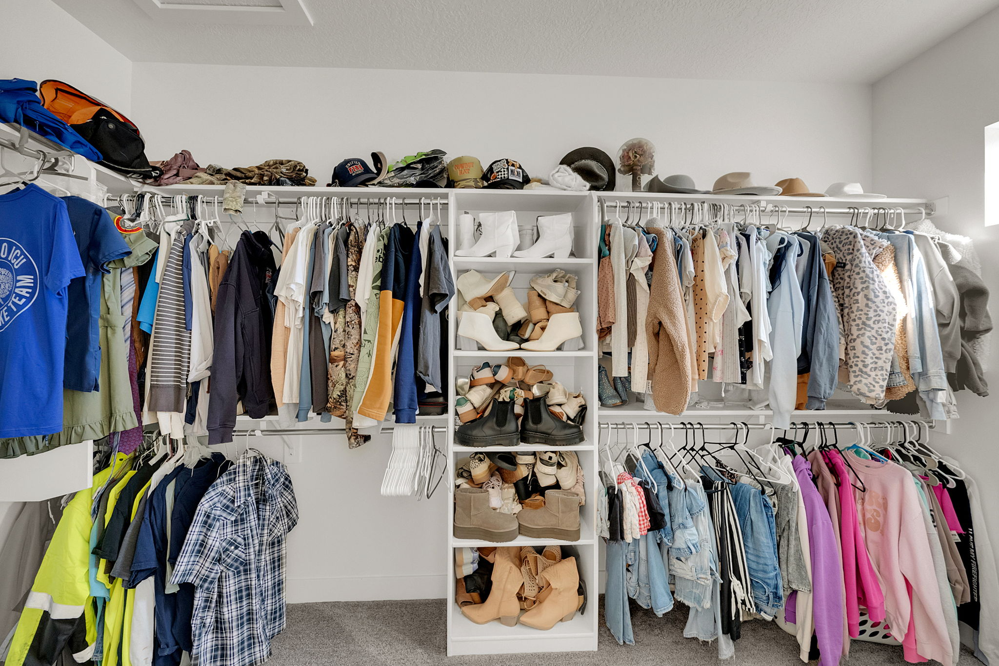 Walk-in closet featuring white wire shelving, built-in white cabinetry with open shelving, multiple clothing rods, and a light gray carpeted floor