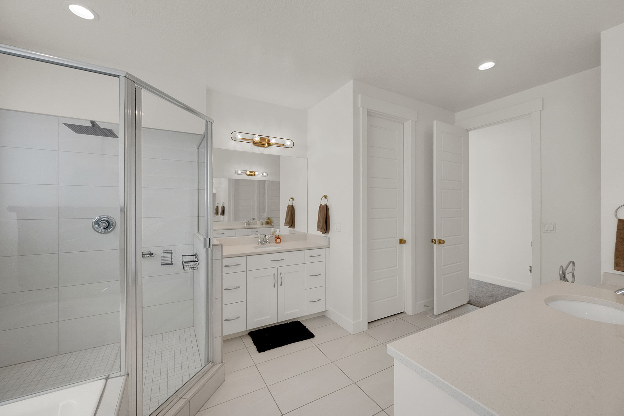 Bathroom featuring a glass-enclosed shower, dual vanity with light-toned countertops, and recessed lighting