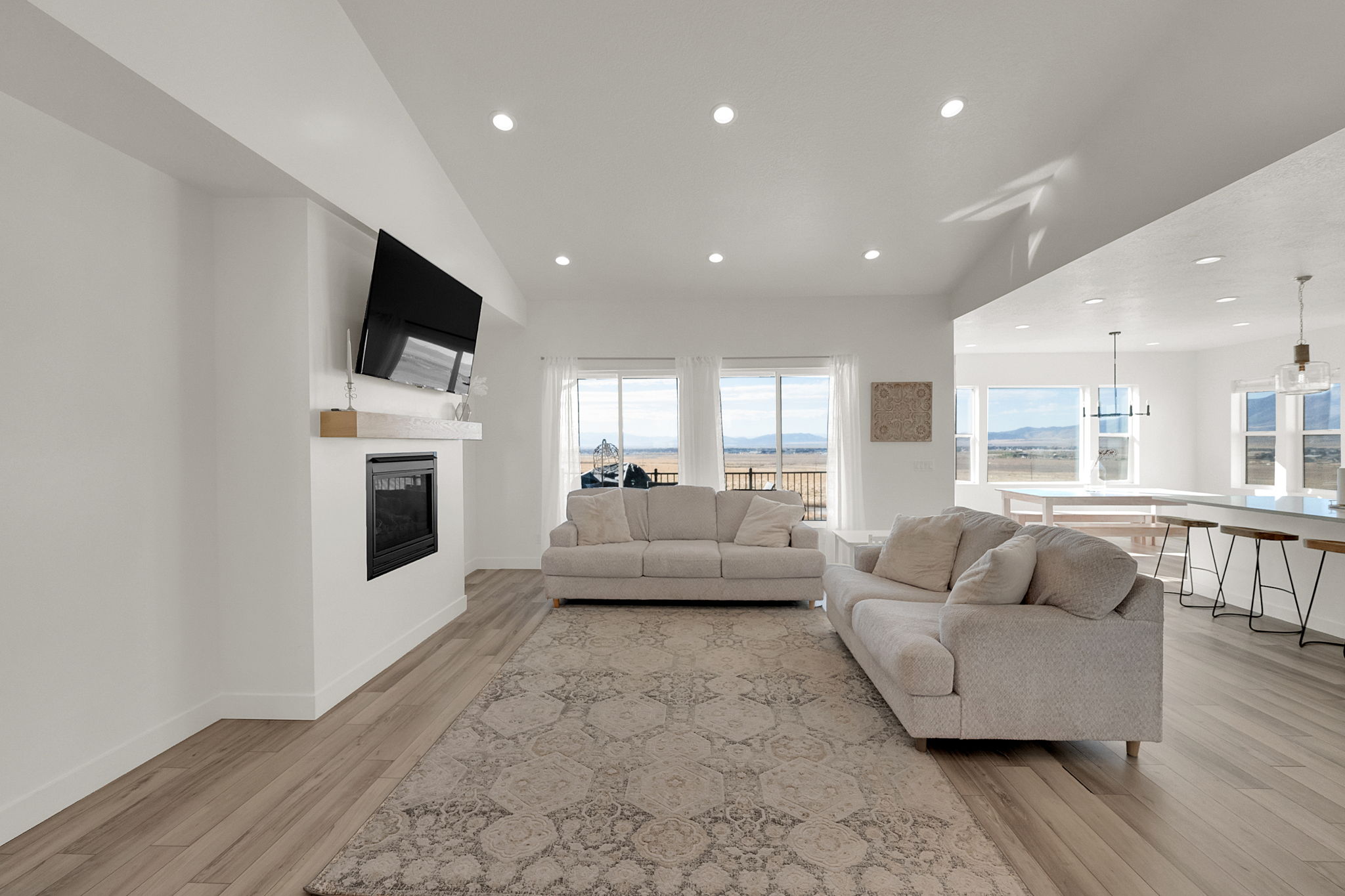 Open concept living area featuring wood-finish flooring, a built-in fireplace with a mantel, recessed ceiling lighting, and large windows with horizontal blinds