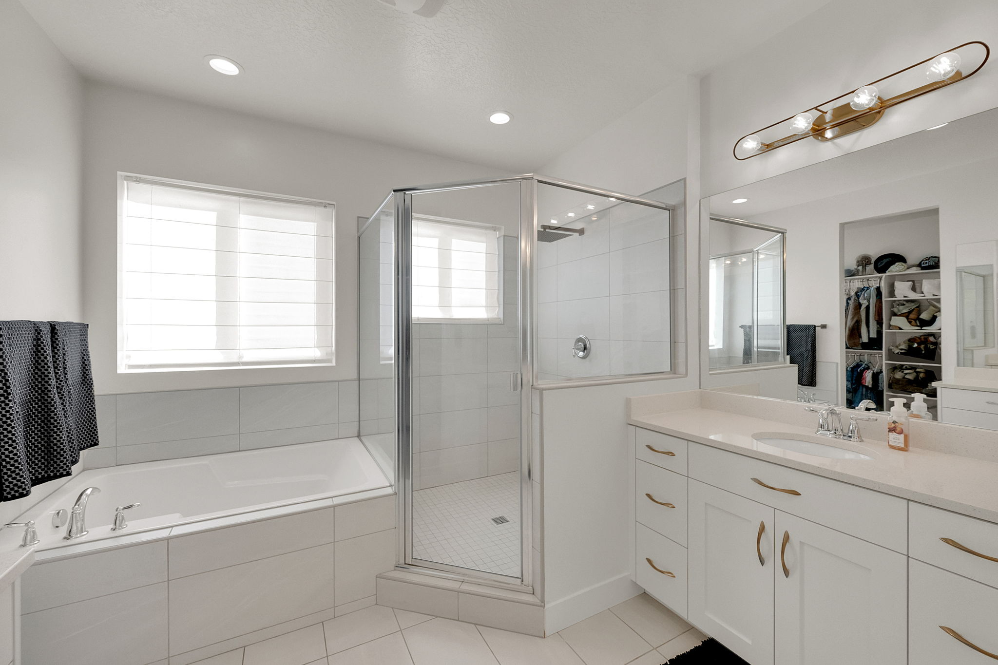 Bright bathroom featuring a glass-enclosed shower, built-in bathtub, and a double vanity with ample storage