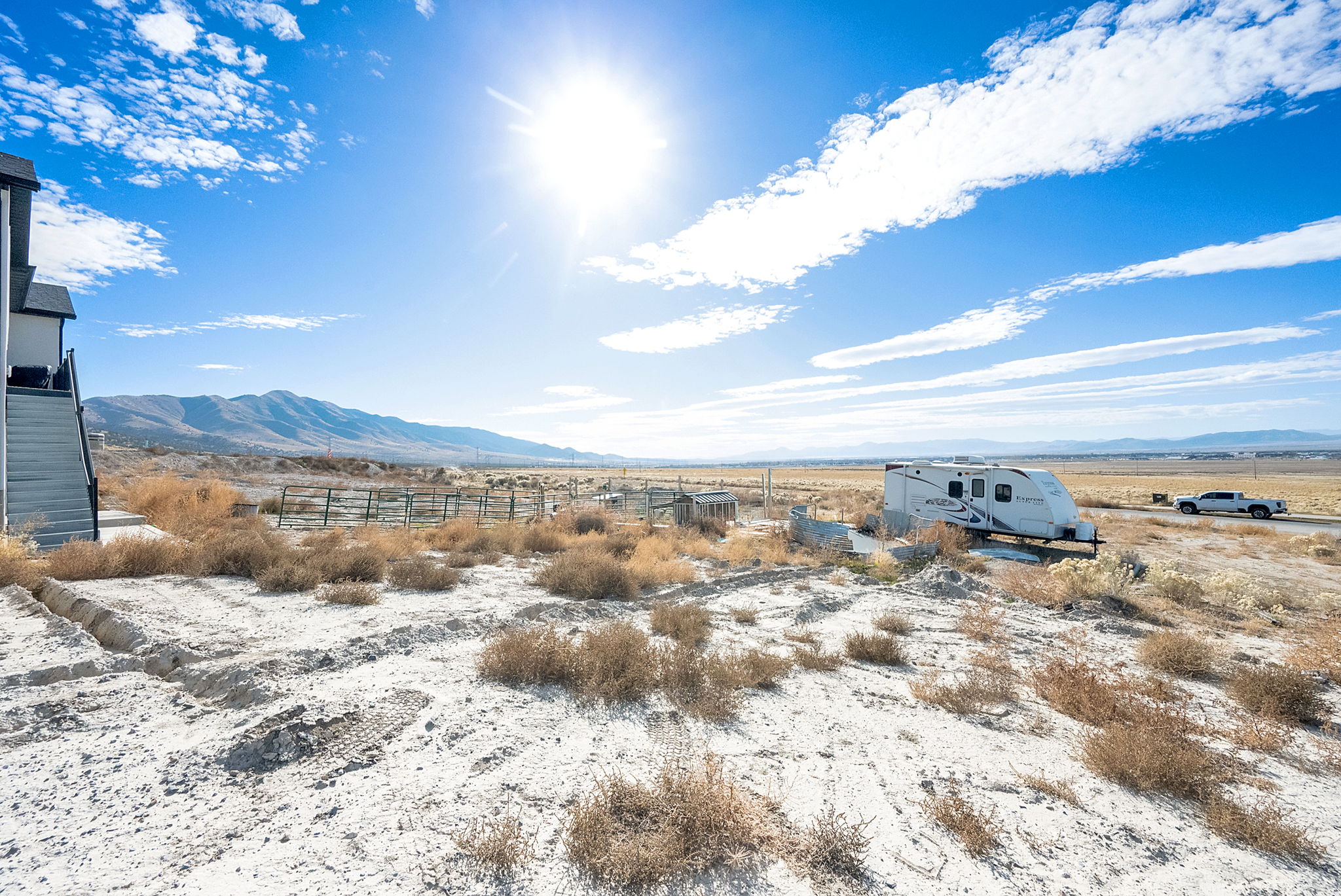 Expansive undeveloped land featuring a partial building exterior with exterior staircase, a distant mountain range, and a visible roadway