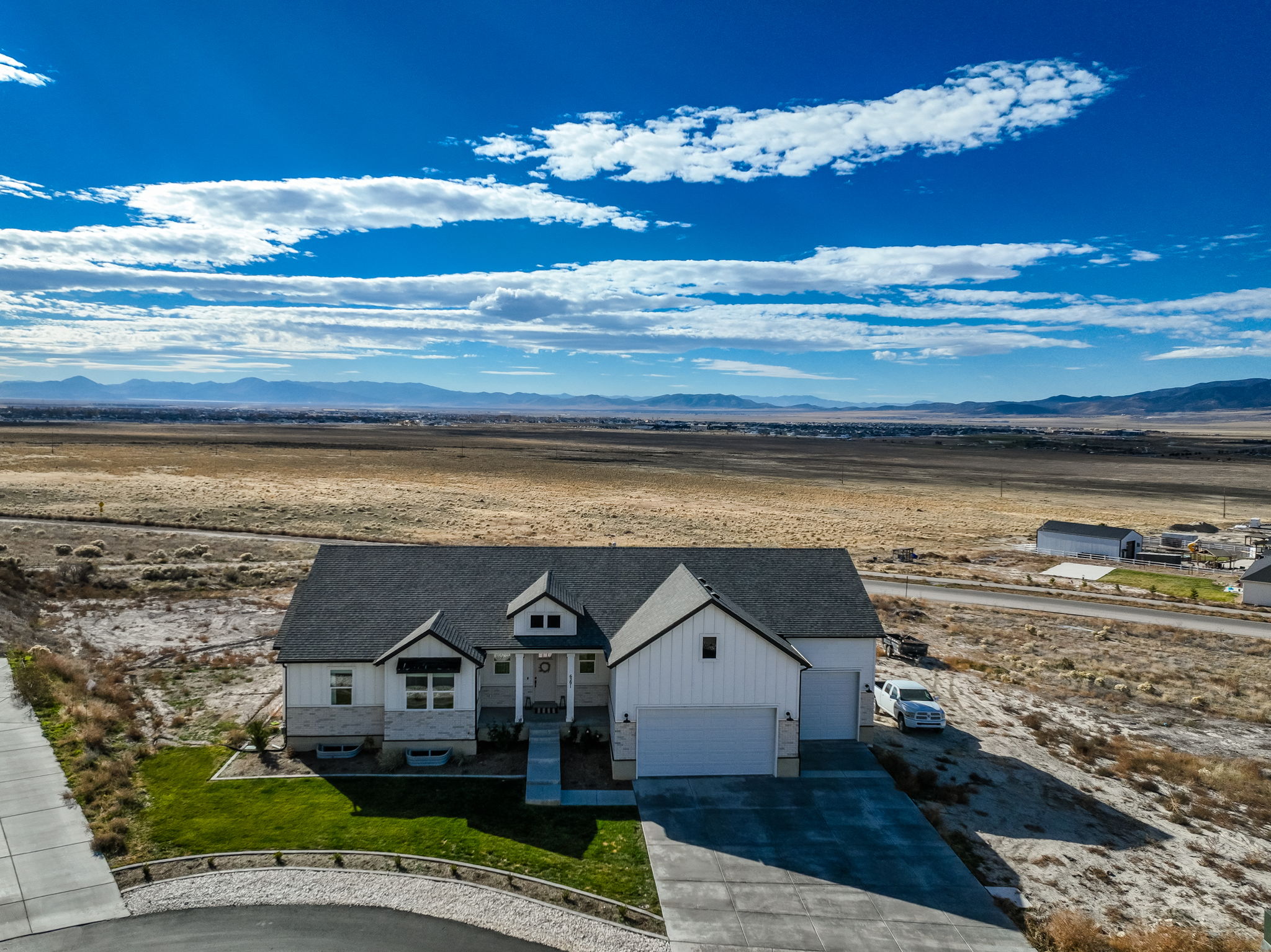 Contemporary farmhouse exterior featuring white vertical siding, light-toned stone accents, and a dark shingled roof