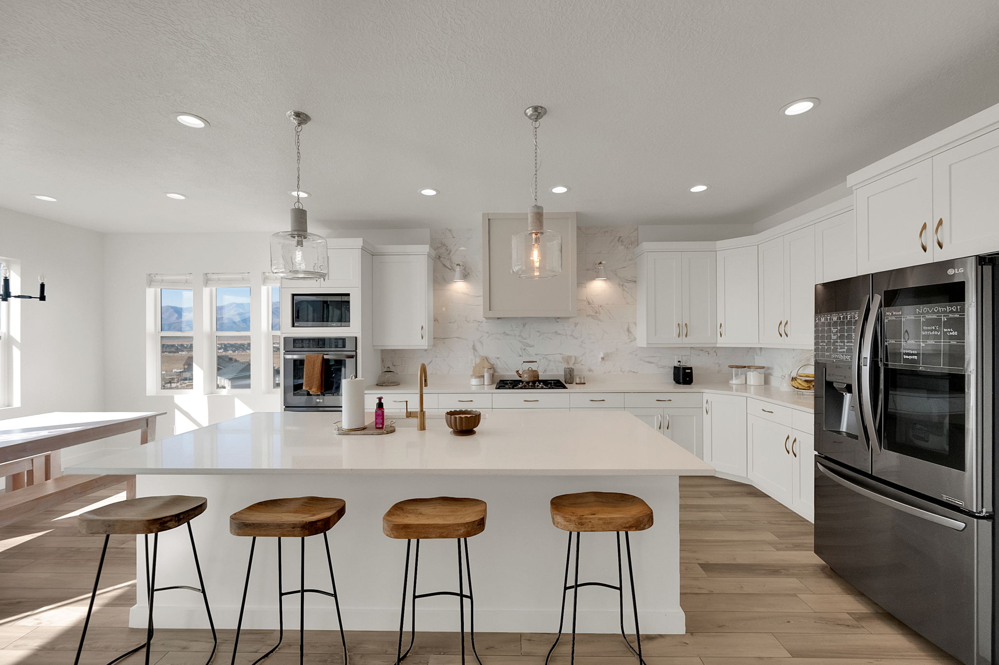 Spacious kitchen featuring an extended island with seating, integrated stainless steel appliances, custom white cabinetry, and recessed lighting