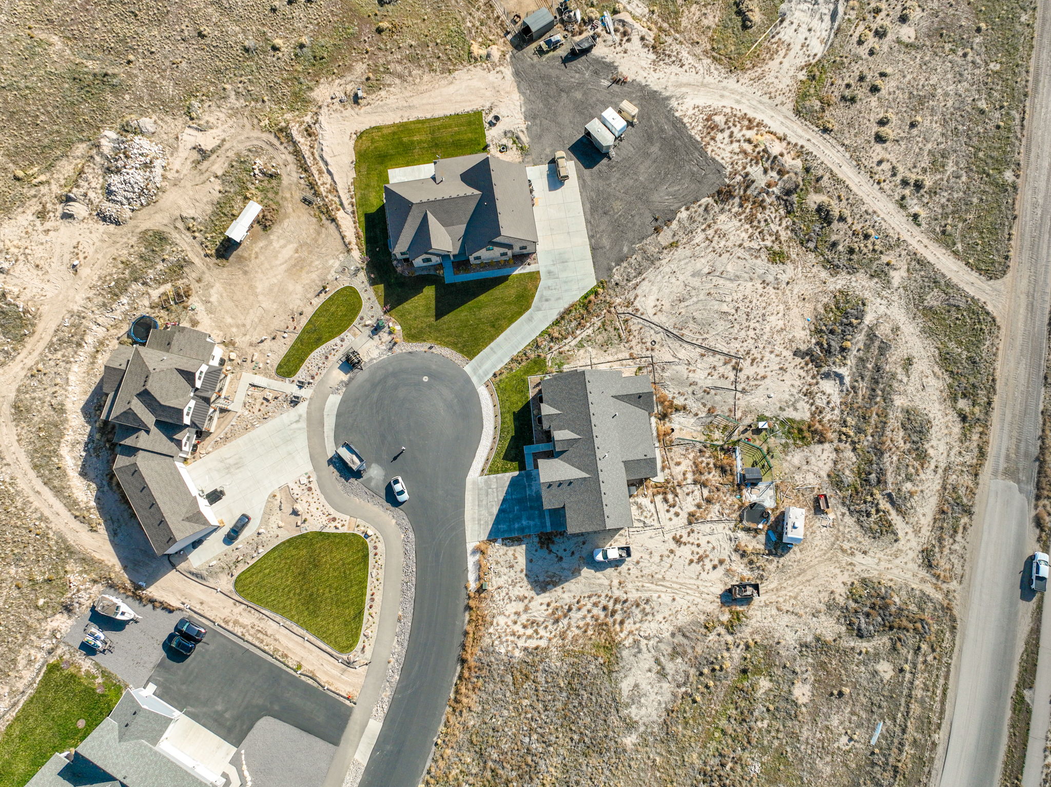 Overhead property view featuring three distinct residences with attached driveways, individual grass patches, and paved street access