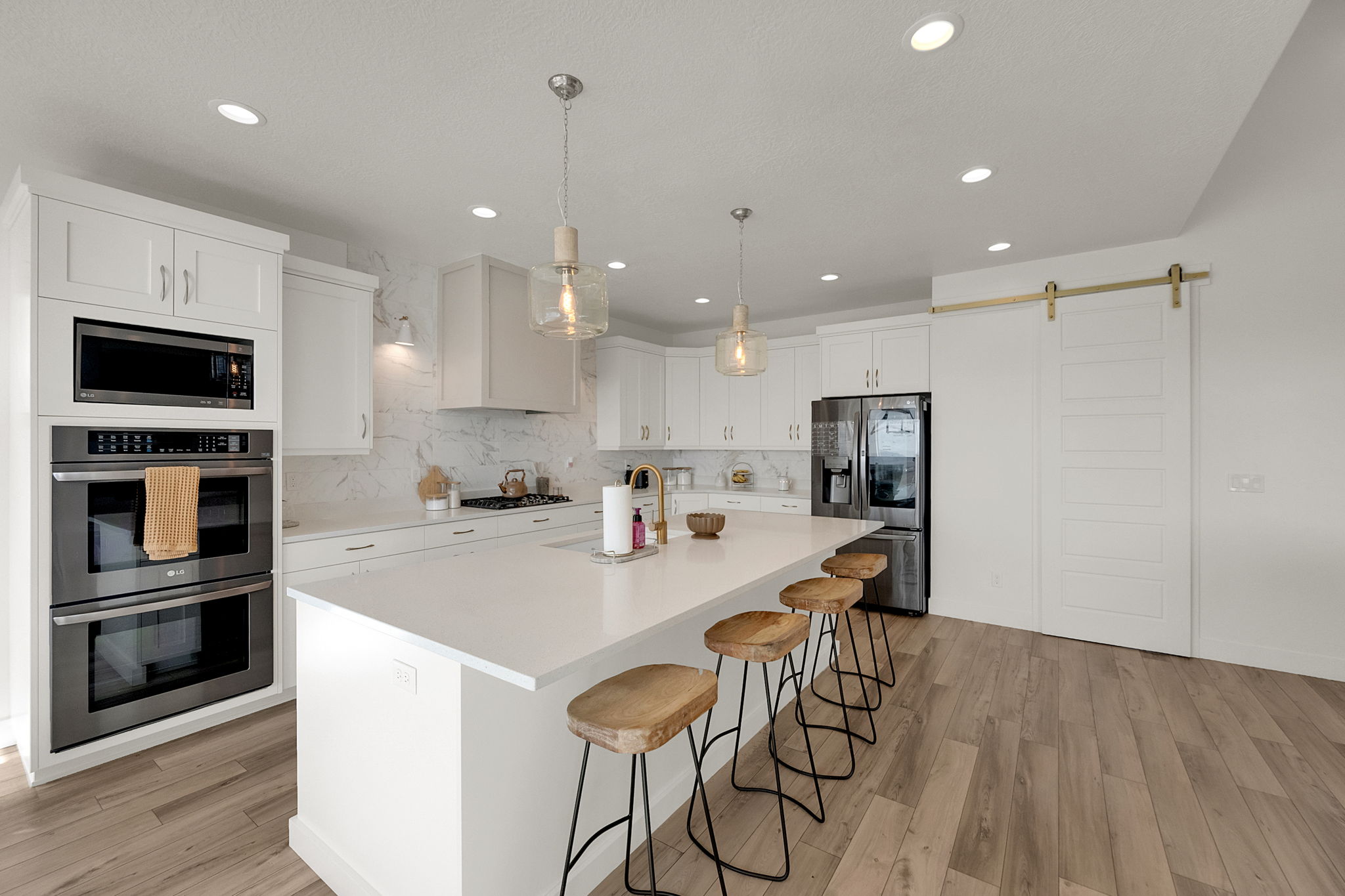 Spacious kitchen featuring an extended island with seating, integrated double ovens, a built-in microwave, wood-finish flooring, and a sliding barn door