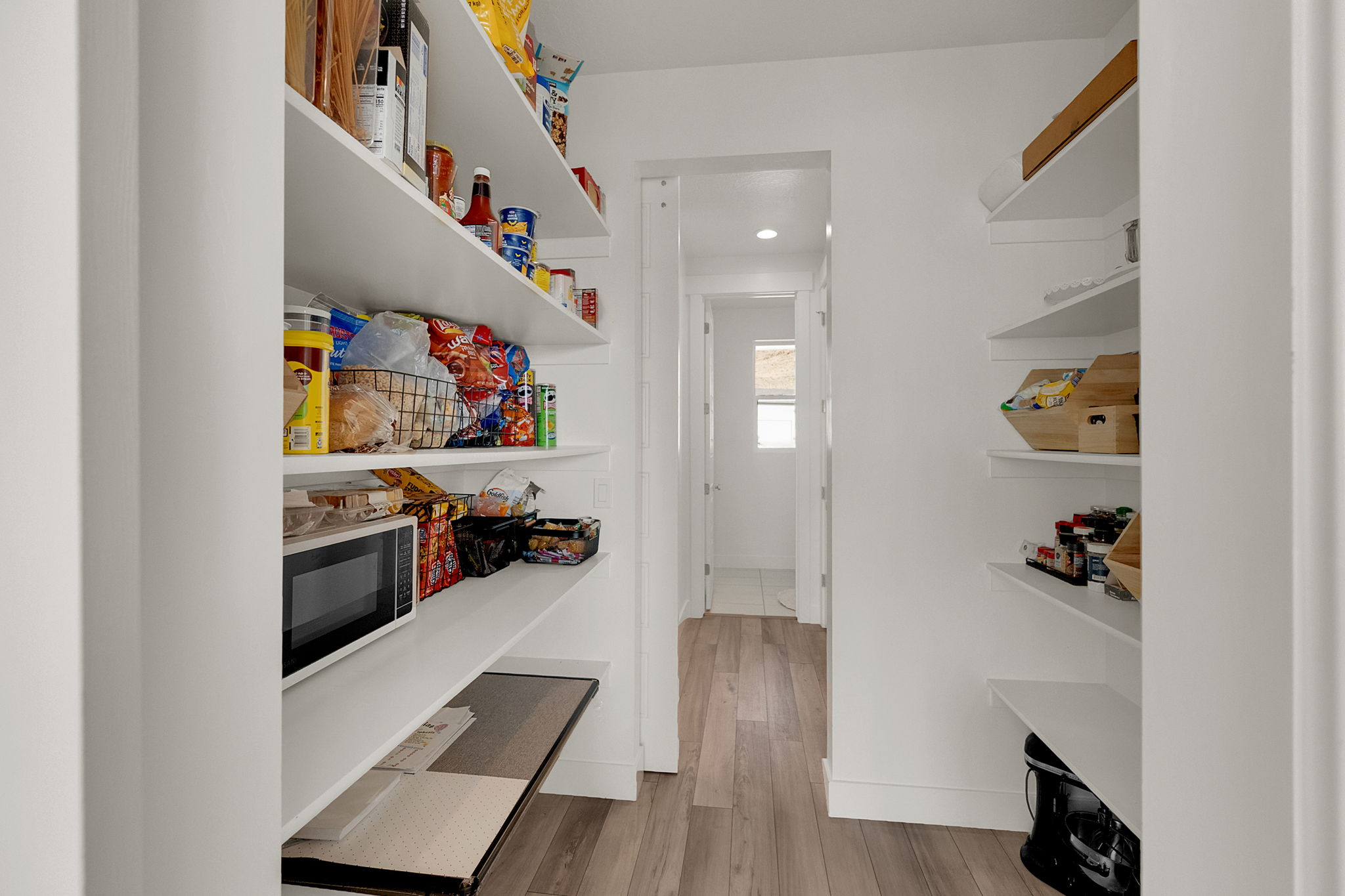 Walk-in pantry featuring extensive built-in shelving, wood-finish flooring, recessed lighting, and a neutral color palette