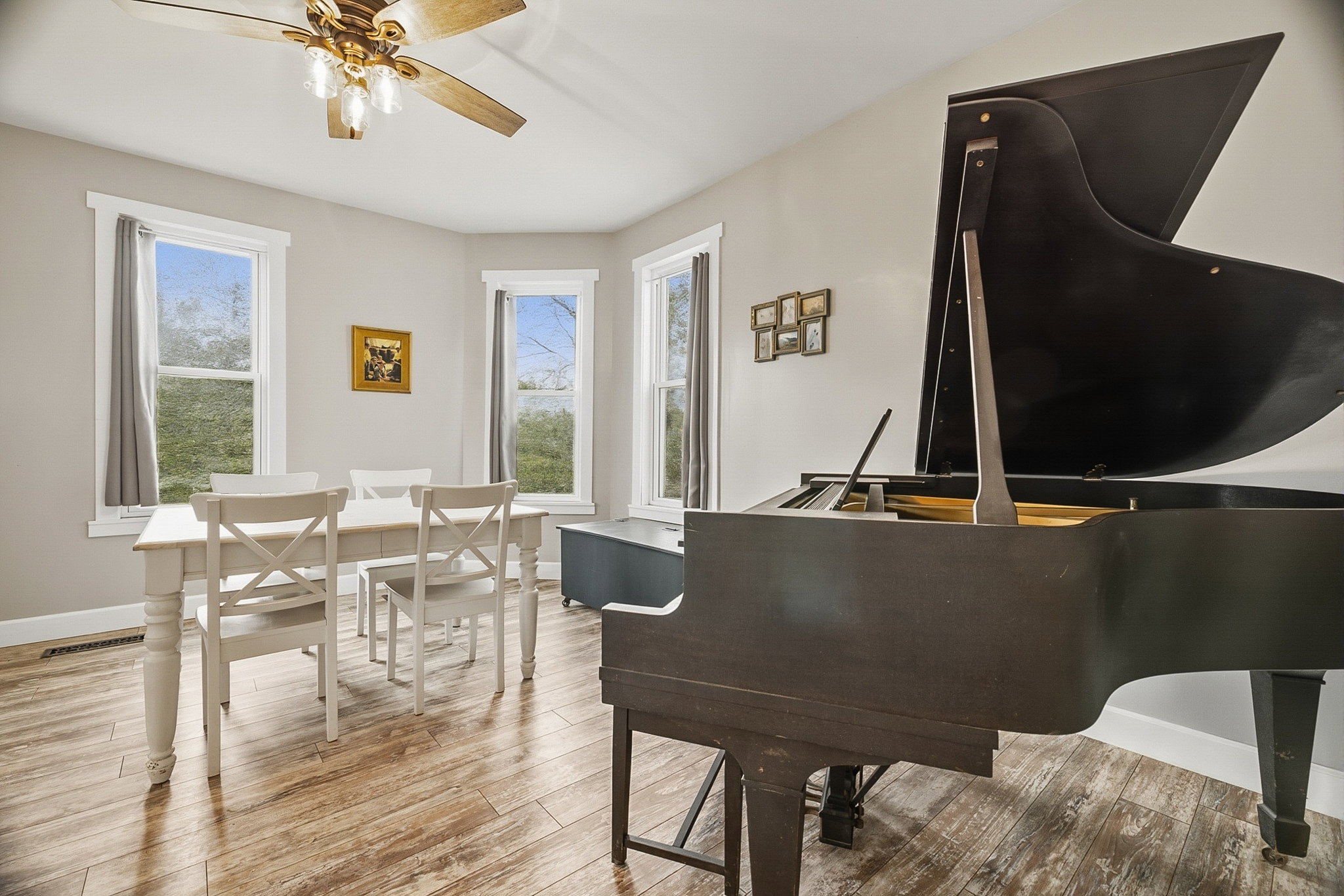 Spacious room featuring light wood-finish flooring, light gray walls, and multiple large windows with white trim