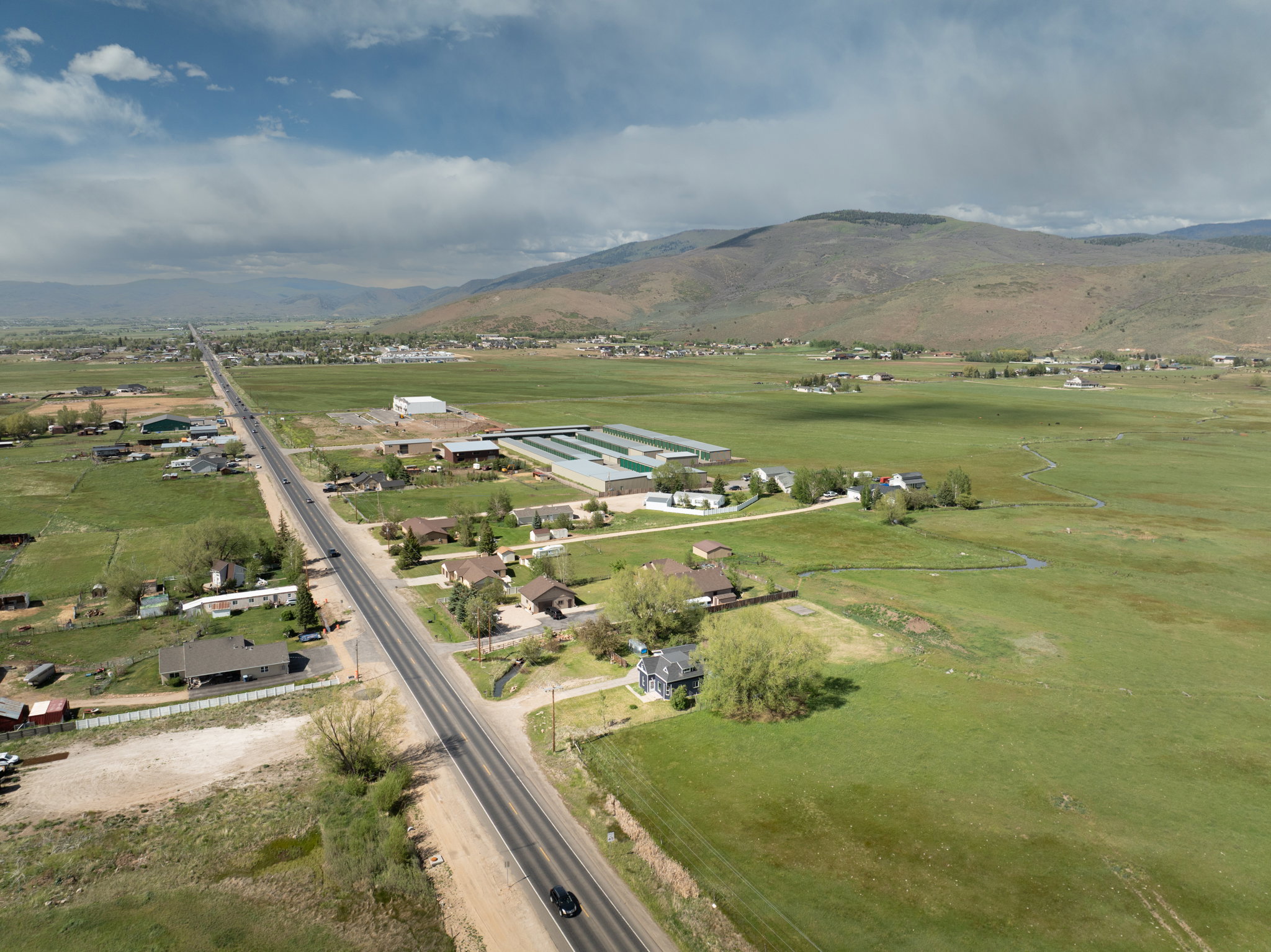 Expansive green fields featuring a long paved road with scattered residential properties