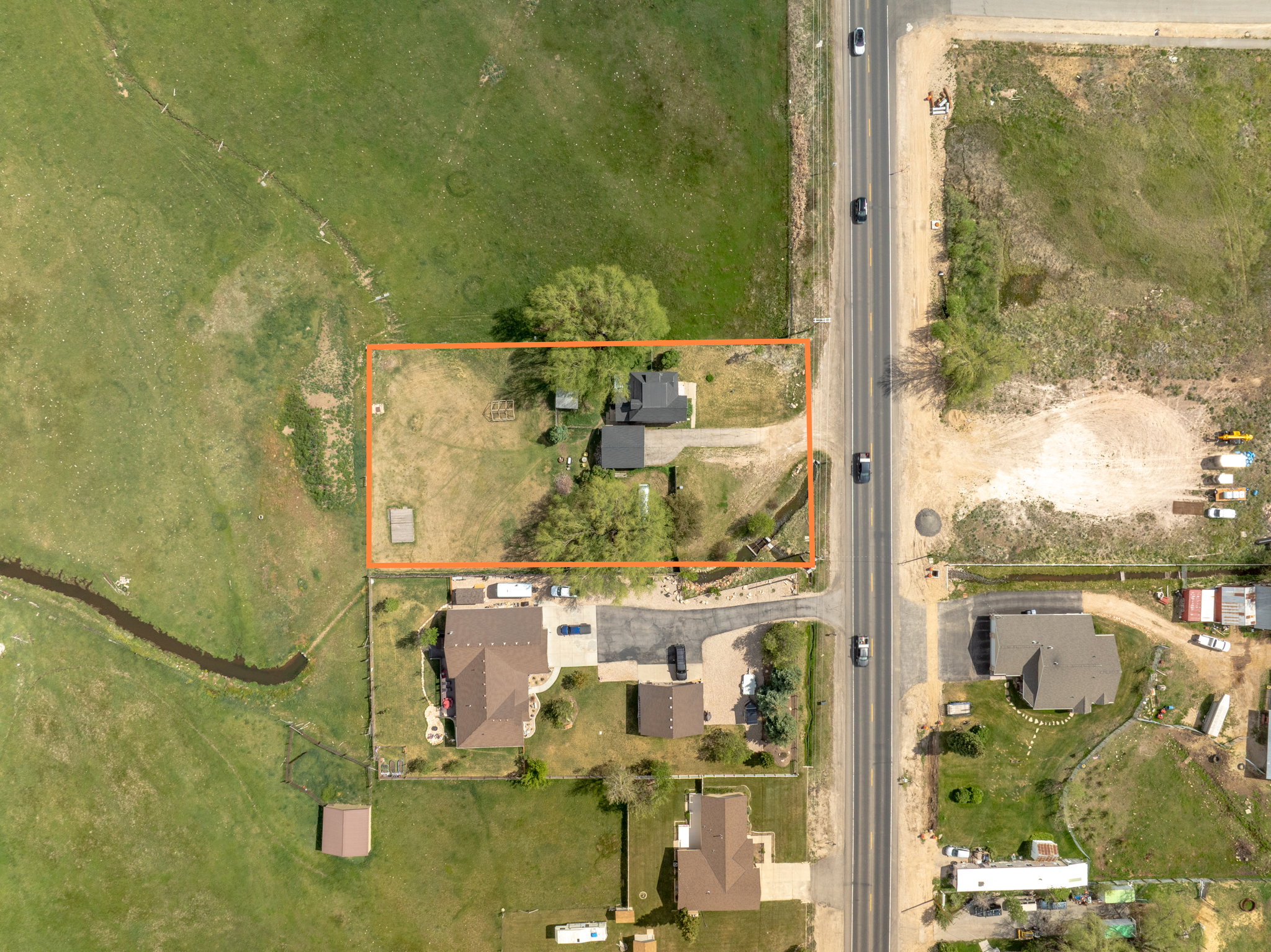 Aerial perspective showcasing a parcel of land with two structures, mature trees, and direct road frontage