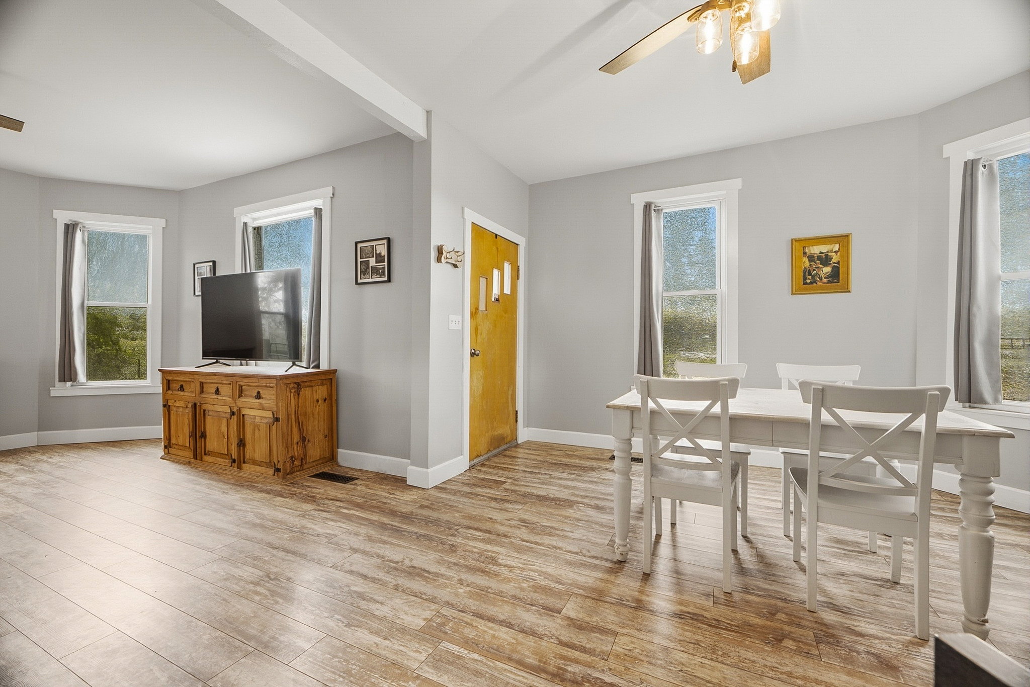 Spacious room with wood-finish flooring, light grey walls, and multiple windows