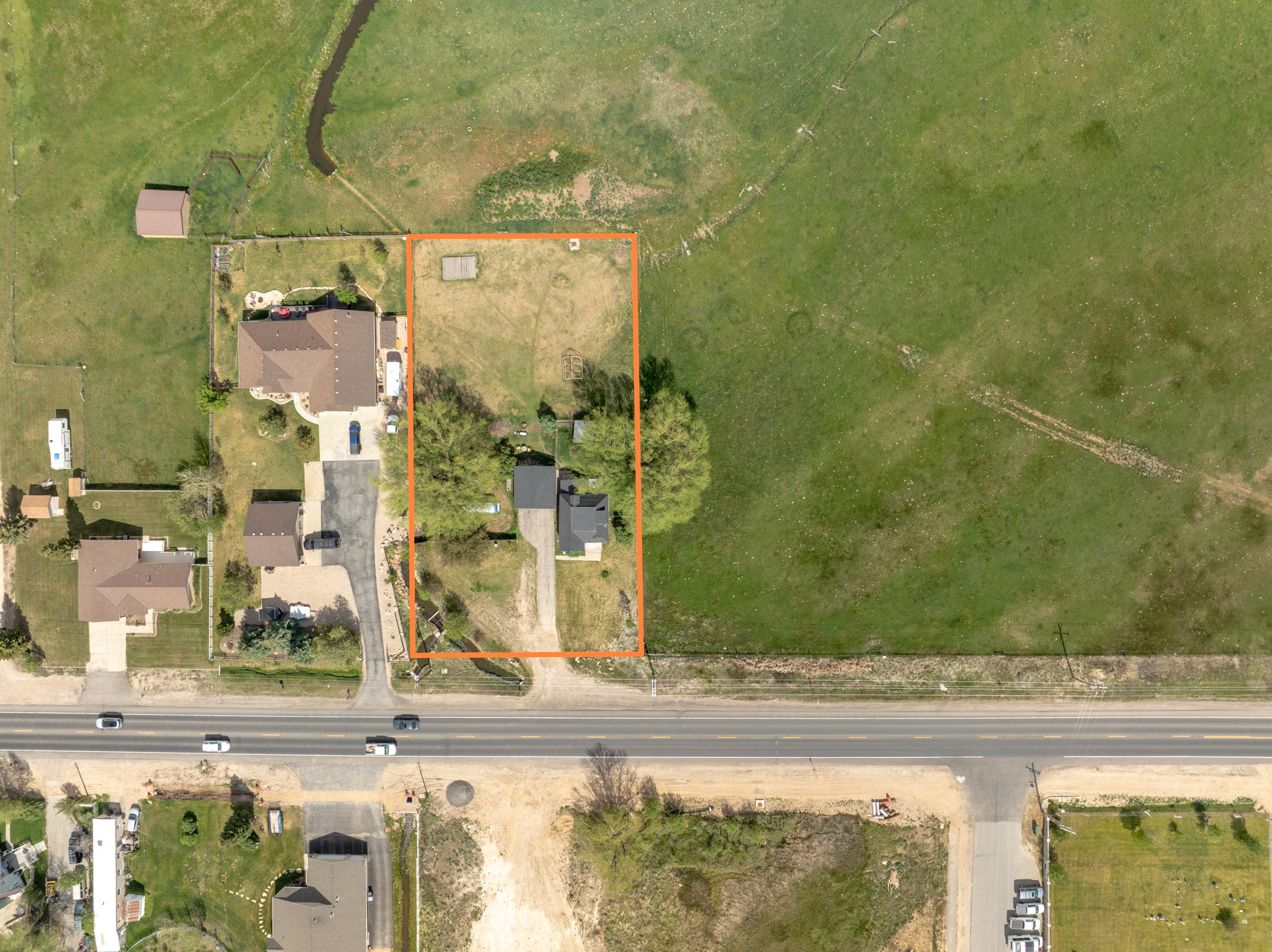Aerial view of a residential property featuring a single-story home with a dark roof and a gravel driveway