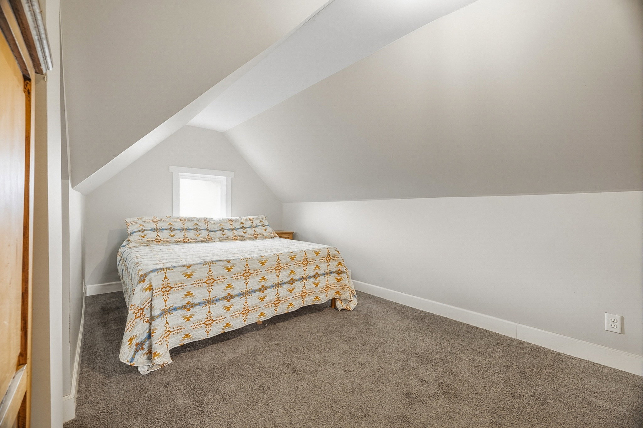 Sloped ceiling room featuring carpet flooring, neutral paint, a single window, and a wood-finish door frame