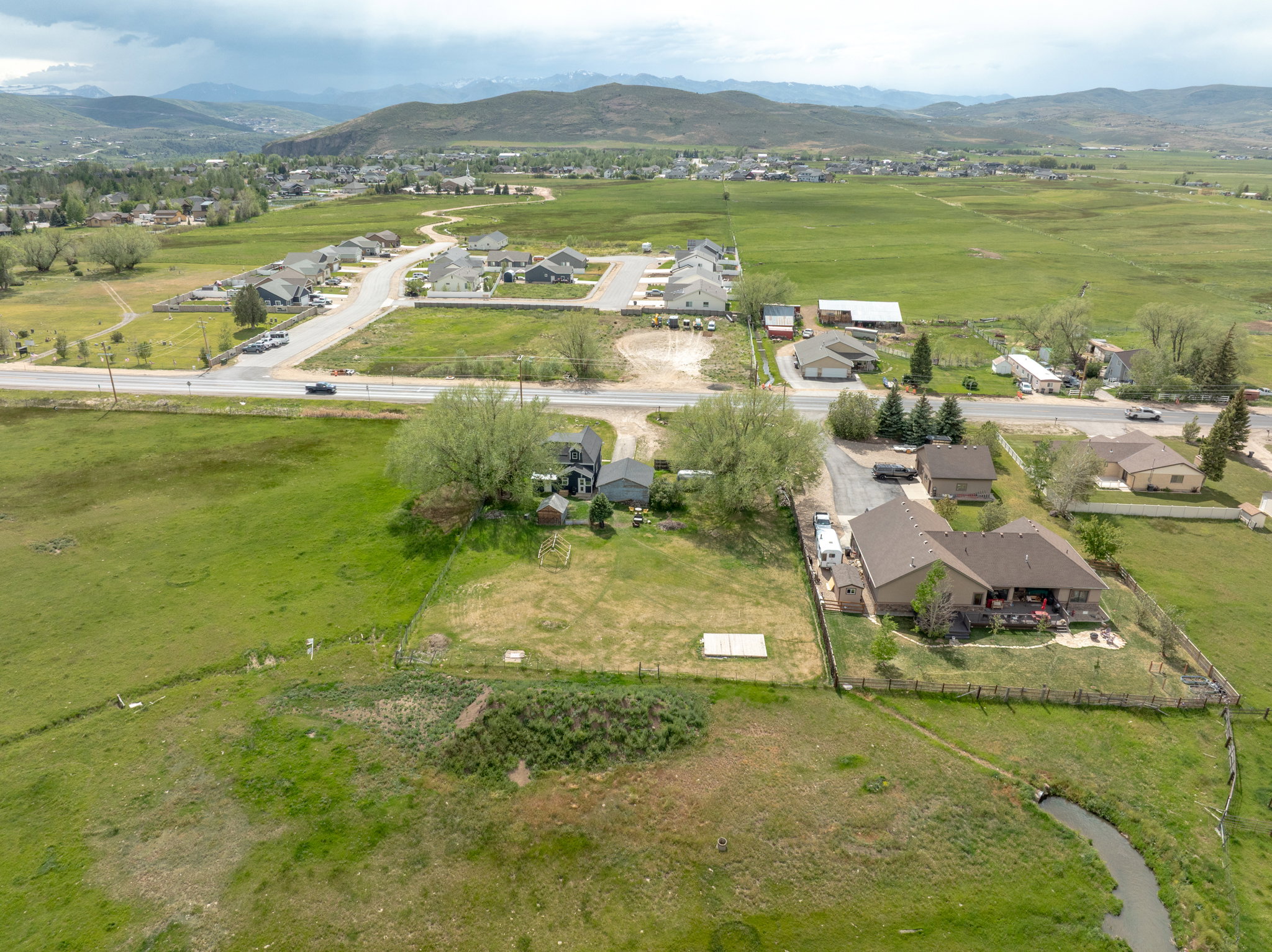 Expansive rural setting with a stream, green fields, and distant mountains