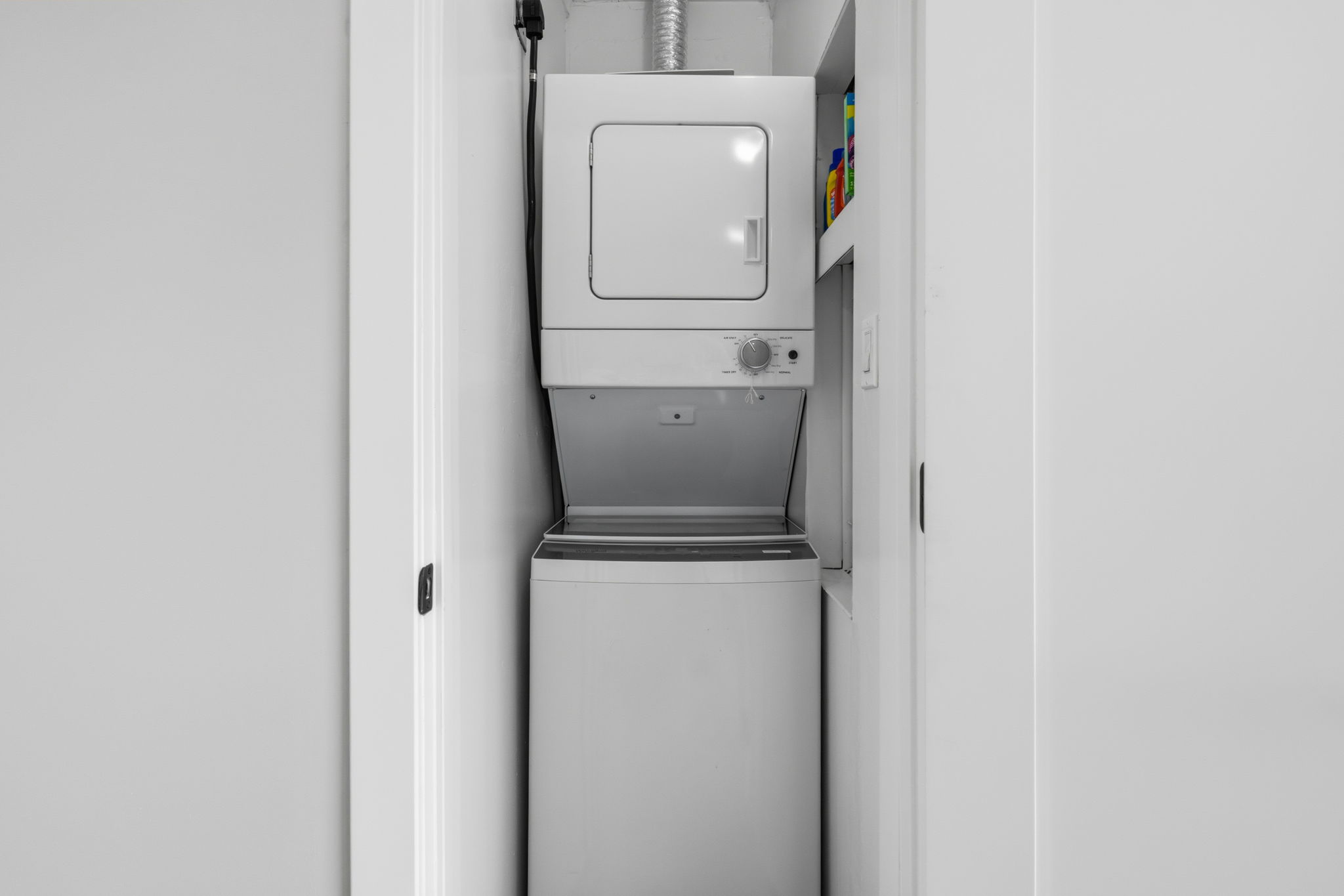Upstairs  laundry closet featuring a stackable washer and dryer, white shelving,