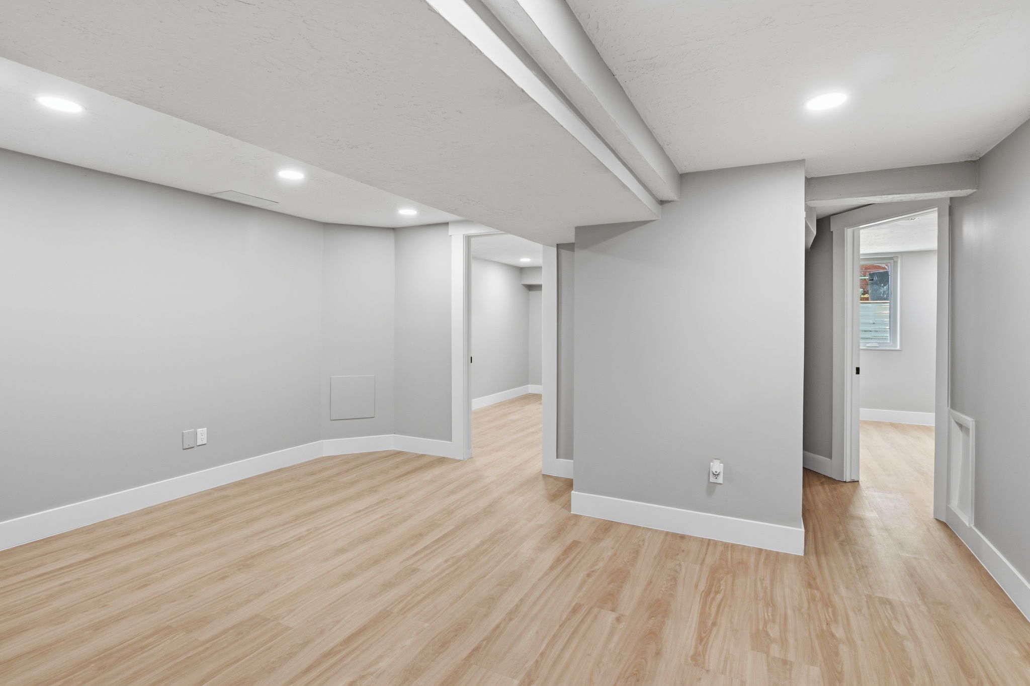 Spacious interior room featuring wood-finish flooring, recessed lighting, neutral wall tones, white baseboards, and doorways leading to additional rooms