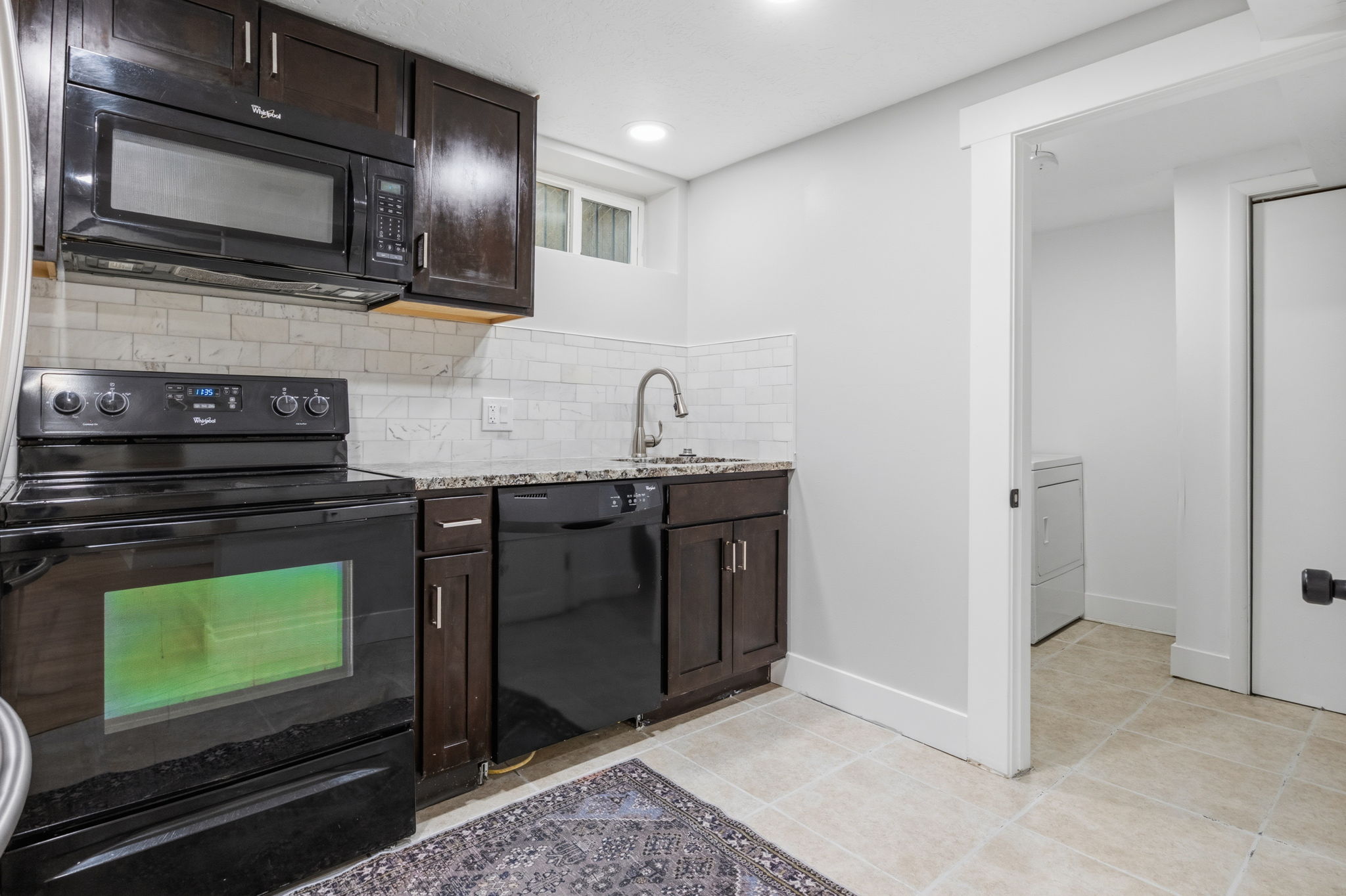 Basement Compact kitchen featuring dark wood-finish cabinetry, granite-style countertops, and subway tile backsplash