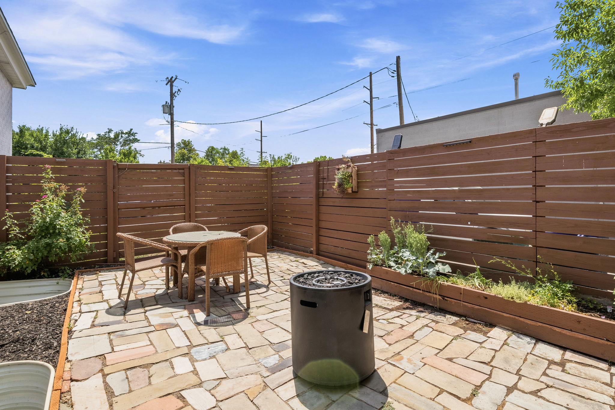 Private fenced patio featuring stone paver flooring, horizontal plank fencing, and a built-in planter box