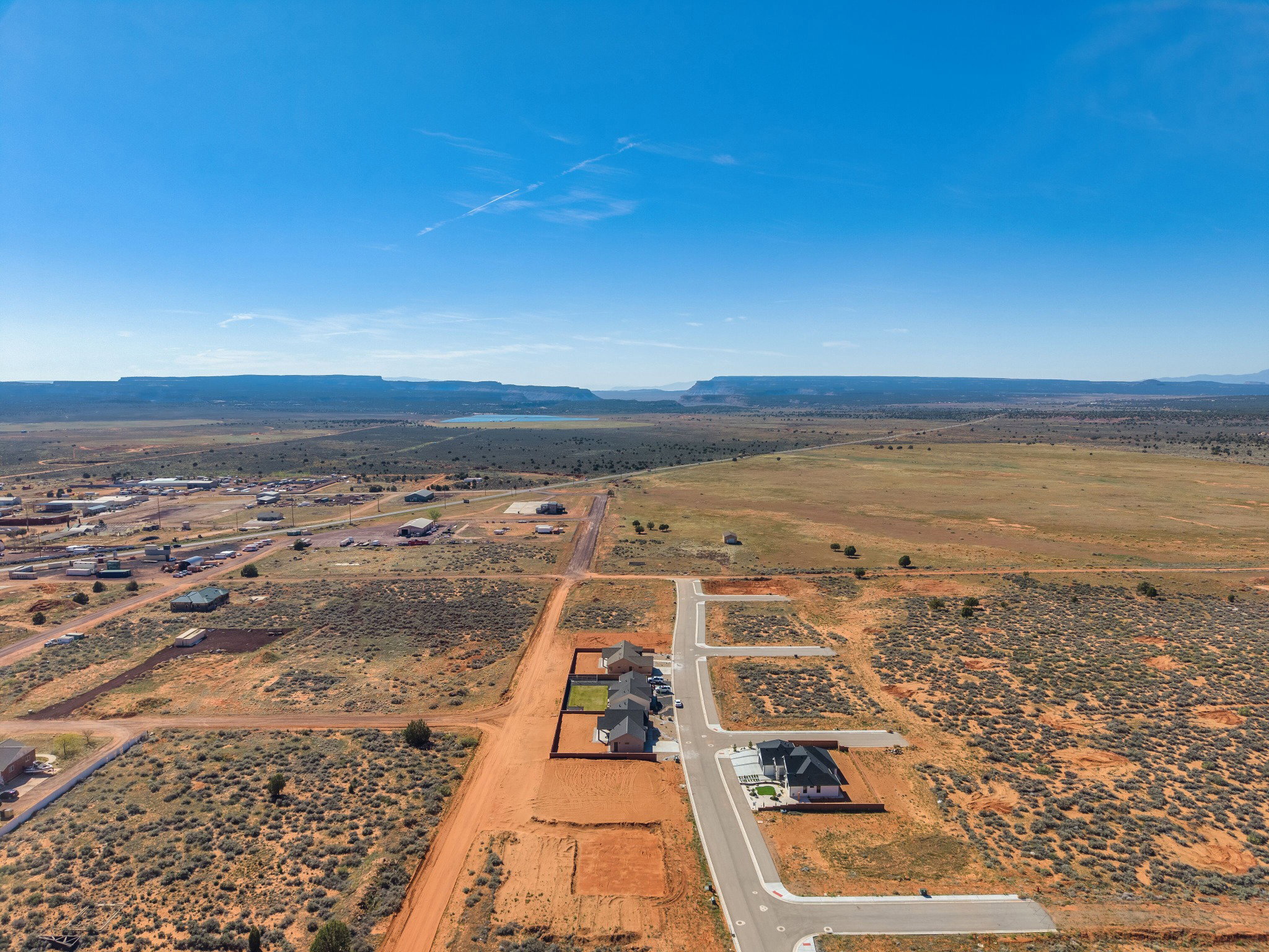 Expansive desert landscape featuring numerous undeveloped lots, a newly paved roadway, and residential structures