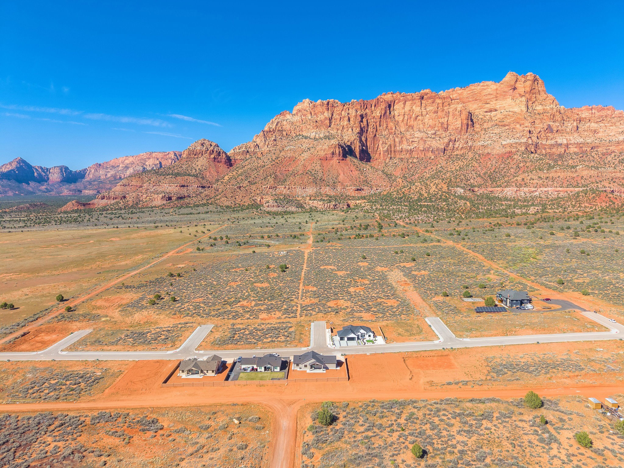 Expansive desert landscape featuring red rock mountain formations and multiple residential lots with paved road access