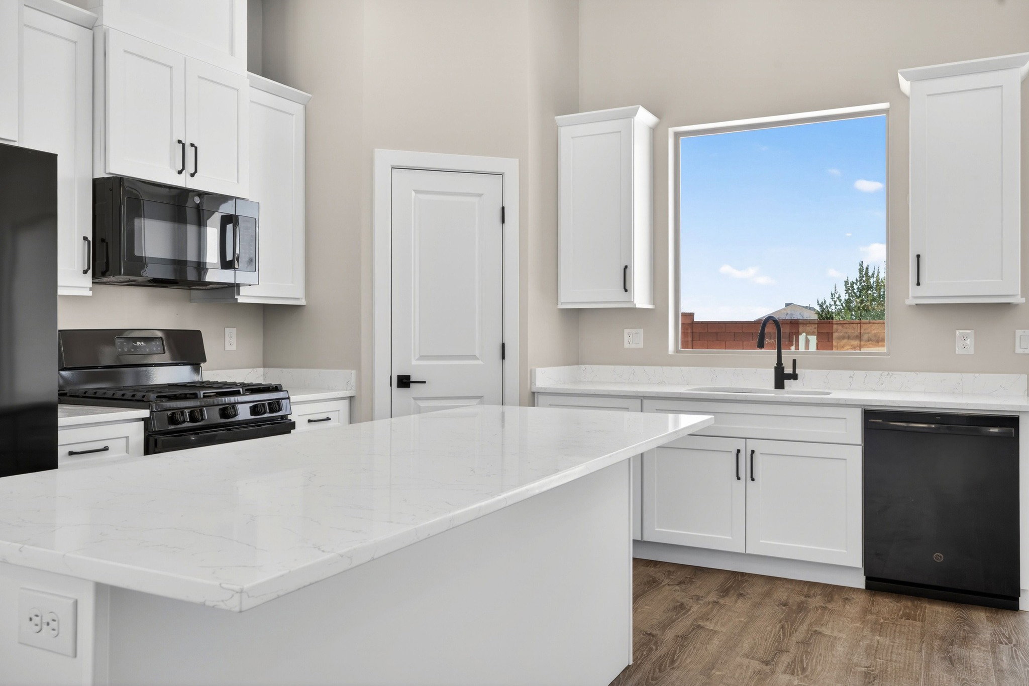 Kitchen featuring white shaker cabinetry, white countertops, a central island, wood-finish flooring, and black appliances including a gas range and built-in microwave