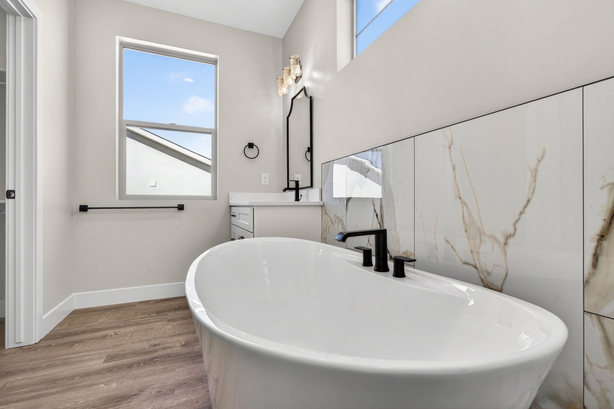 Freestanding soaking tub with matte black fixtures, set against a floor-to-ceiling accent wall featuring large format white and gold veined tiles