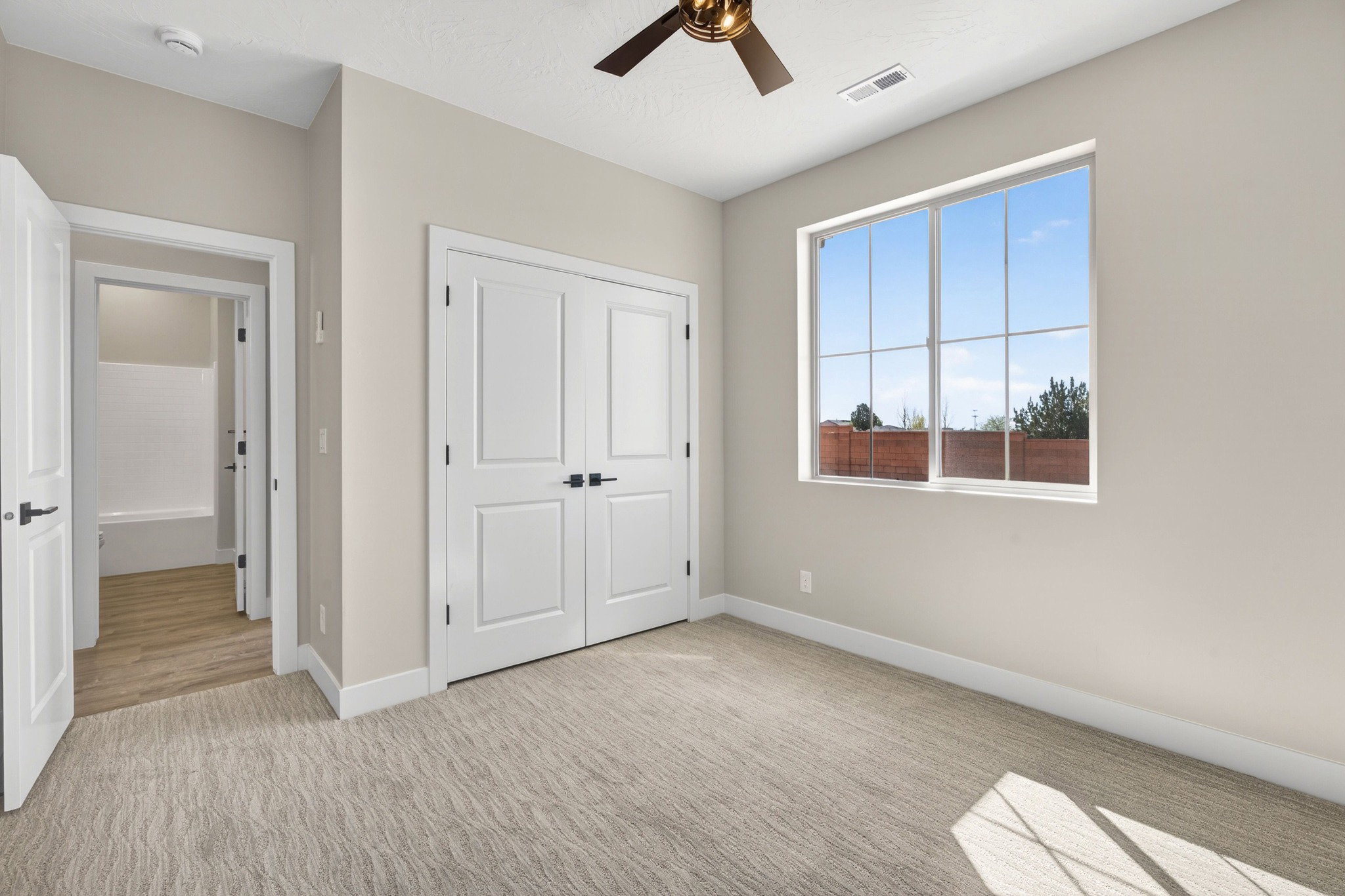 Carpeted room featuring a large window, double-door closet, ceiling fan, and painted trim