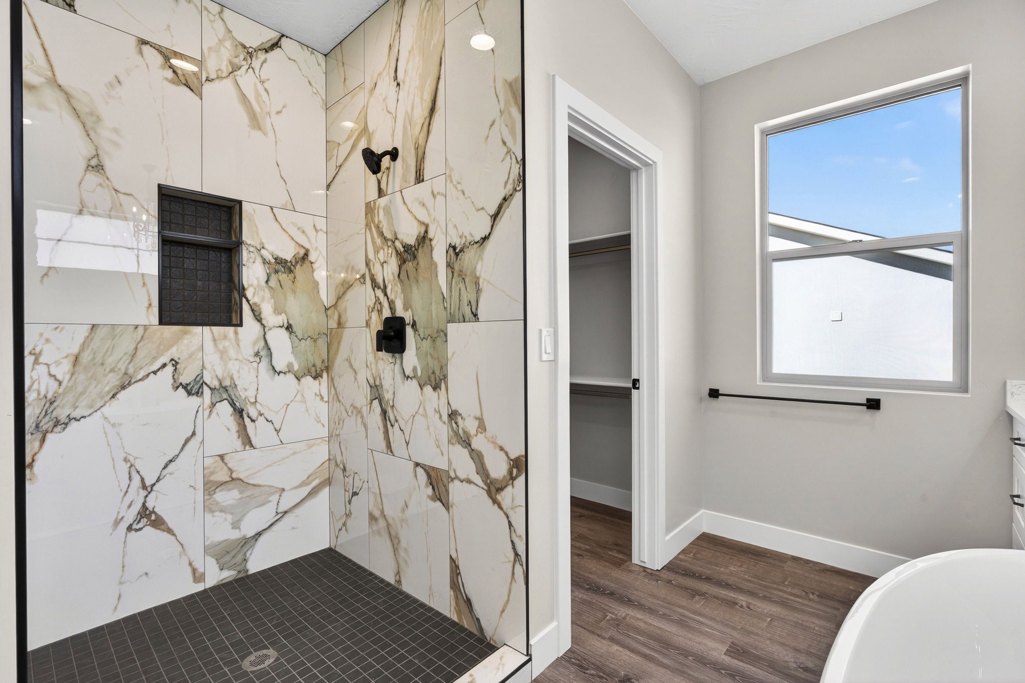 Modern shower with large format marble-look tile walls, a built-in shower niche with dark grid tile, and a dark tile shower pan