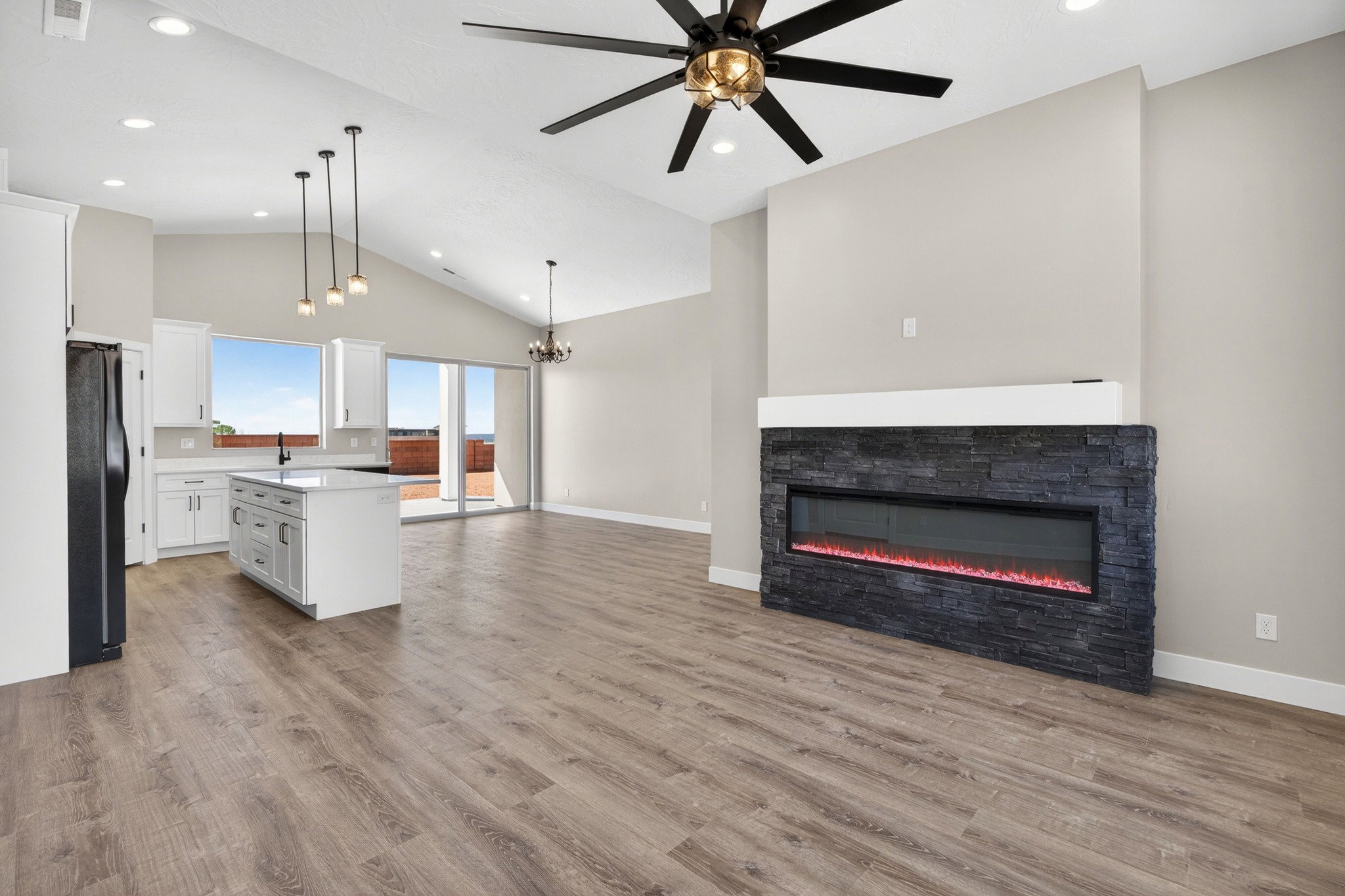 Open-concept living space featuring vaulted ceilings, wood-finish flooring, and a contemporary linear fireplace with stacked stone surround