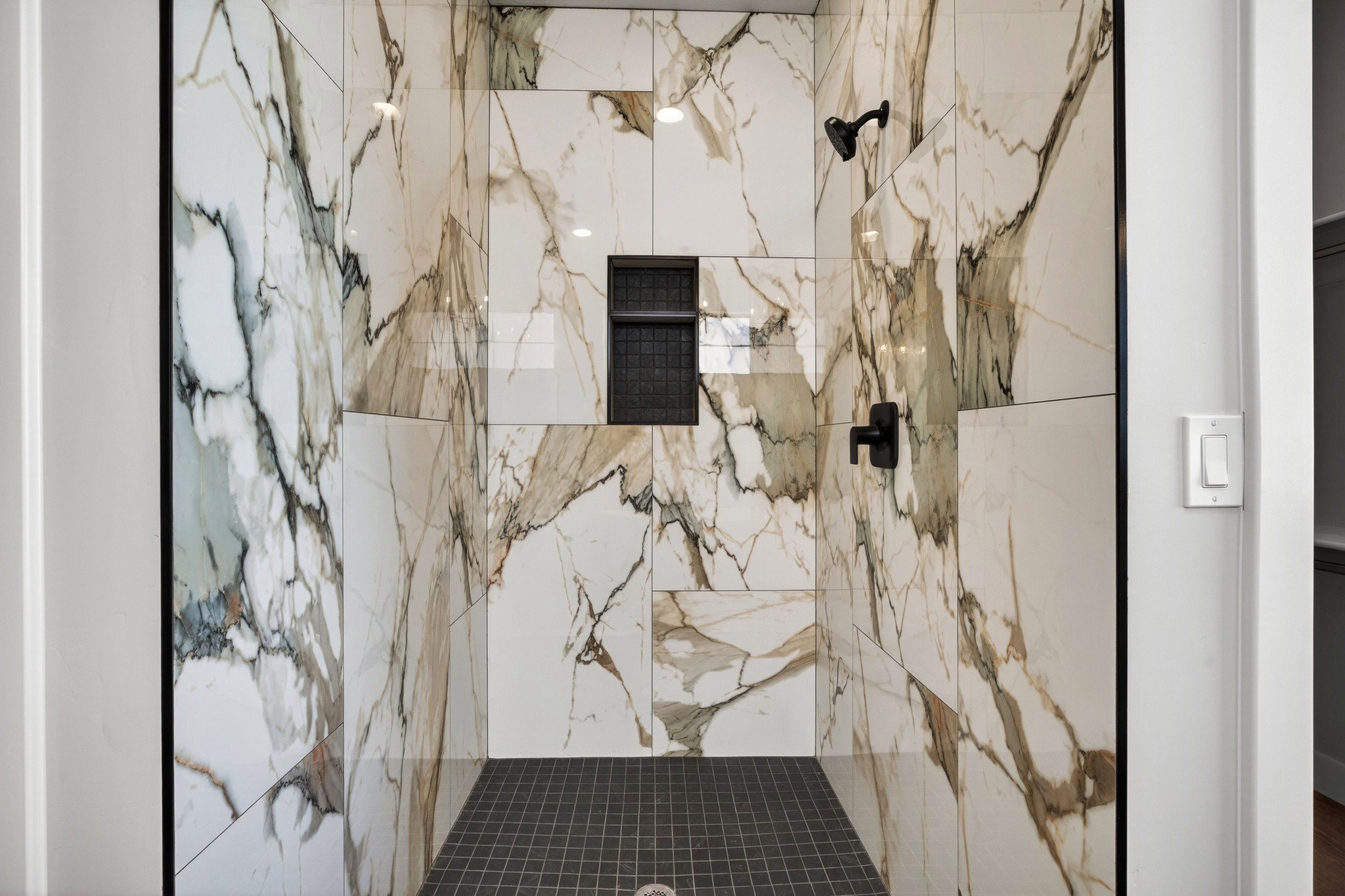 Walk-in shower featuring large format veined wall tiles, a built-in shower niche, and matte black fixtures