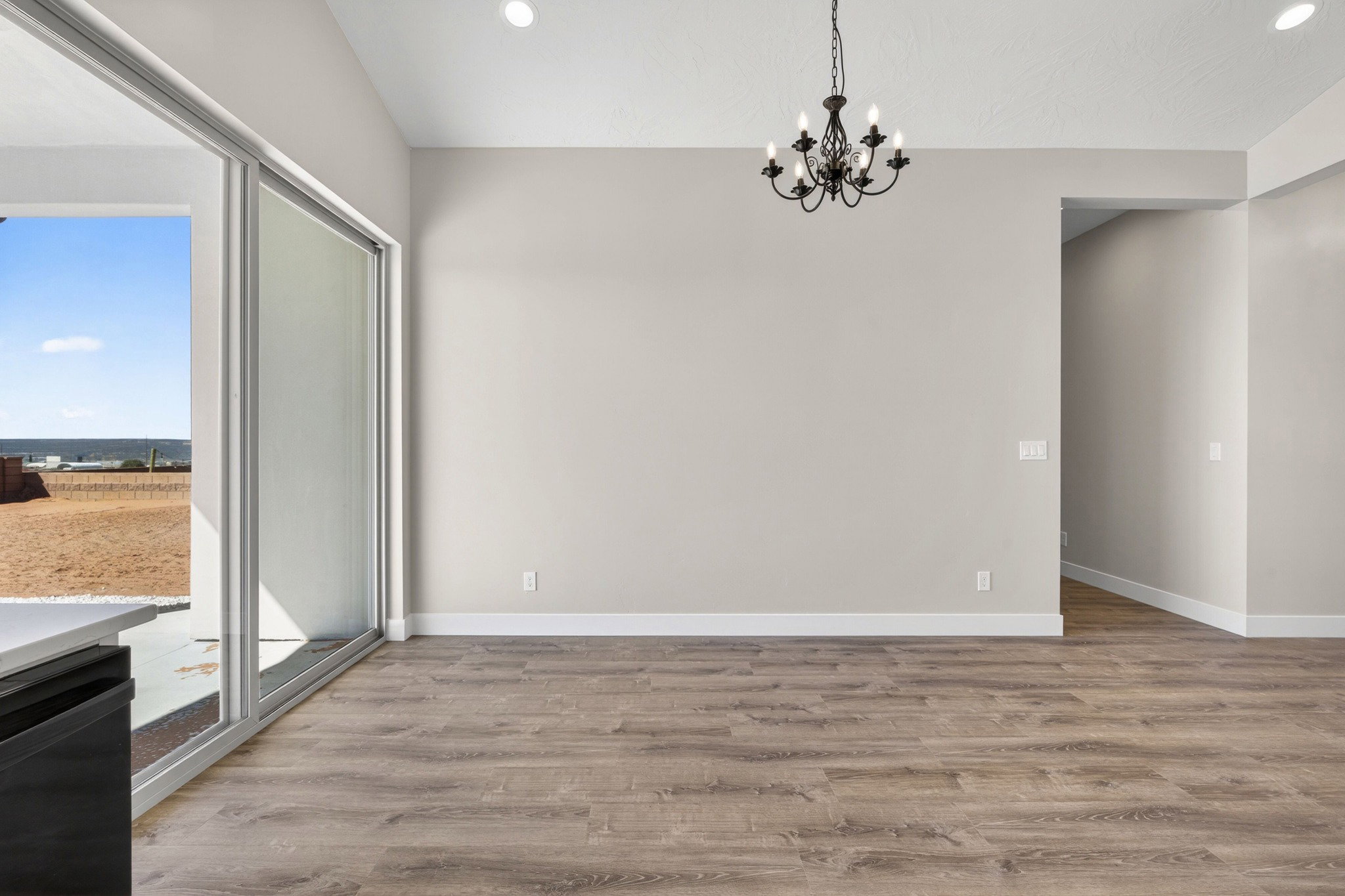 Spacious room featuring wood-finish flooring, light grey wall tones, and a black wrought iron chandelier