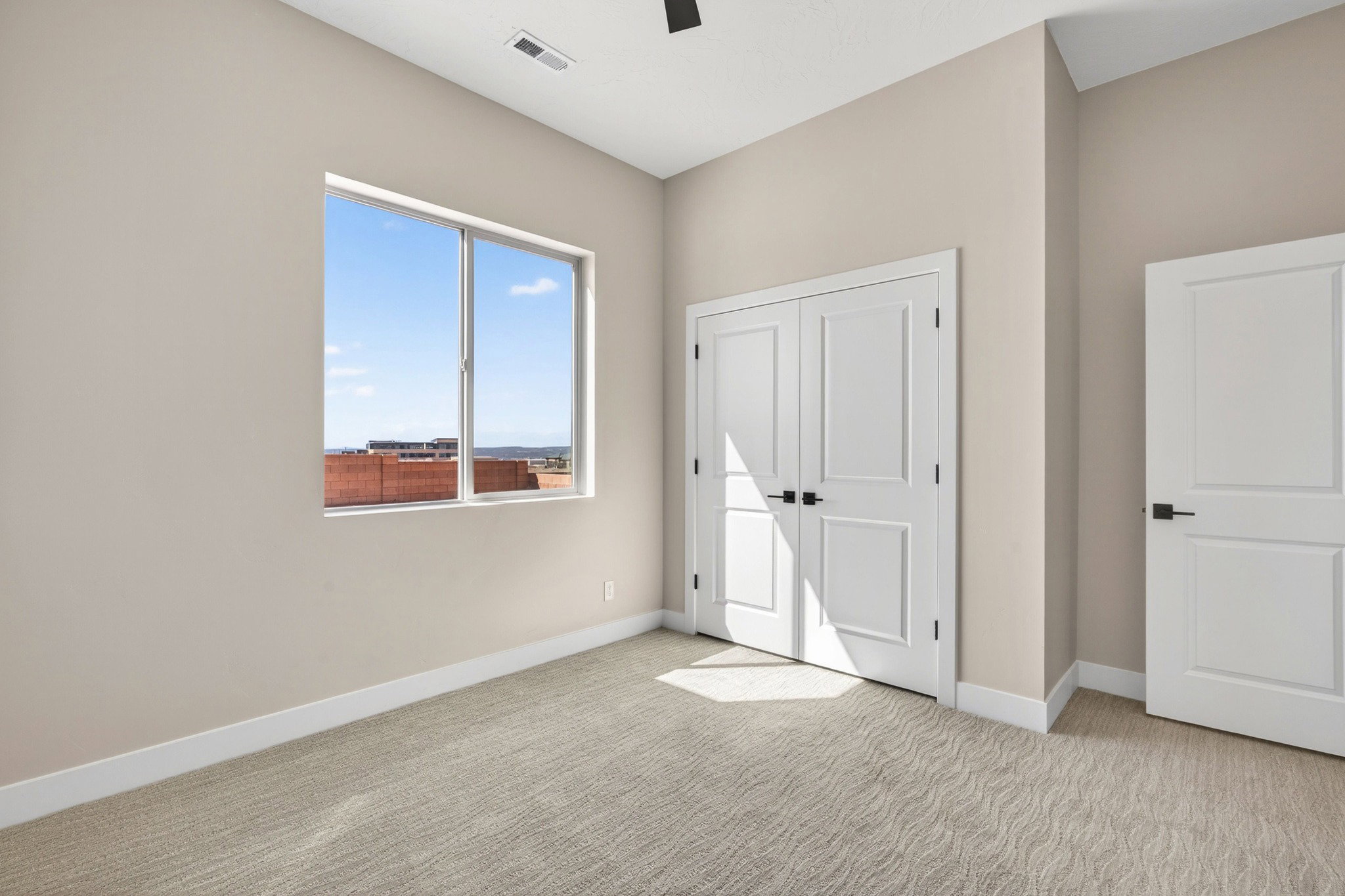 Neutral-toned room featuring a large window, light-colored walls, and textured carpeting