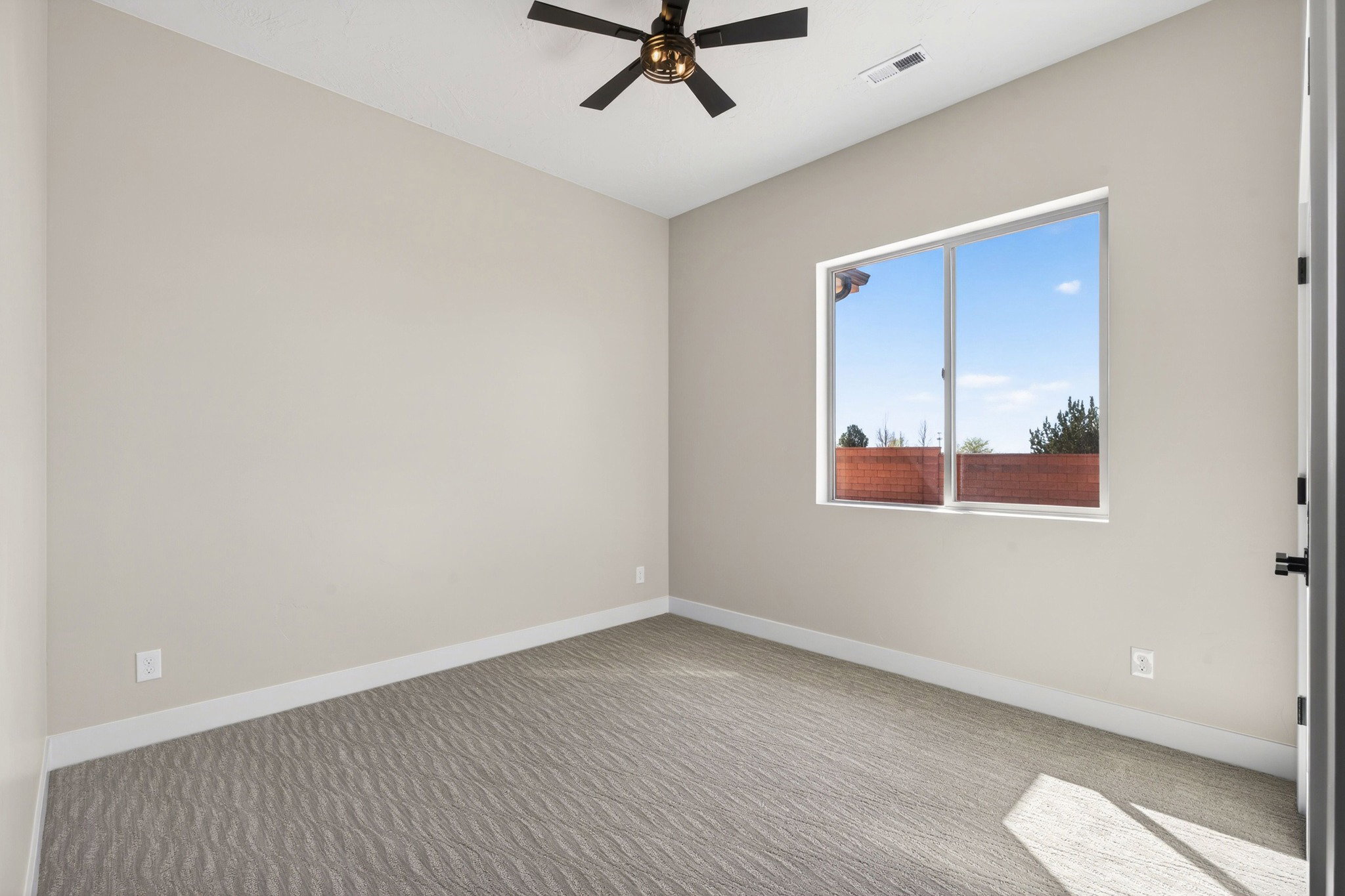Spacious room featuring light-toned walls, patterned carpet flooring, and white trim